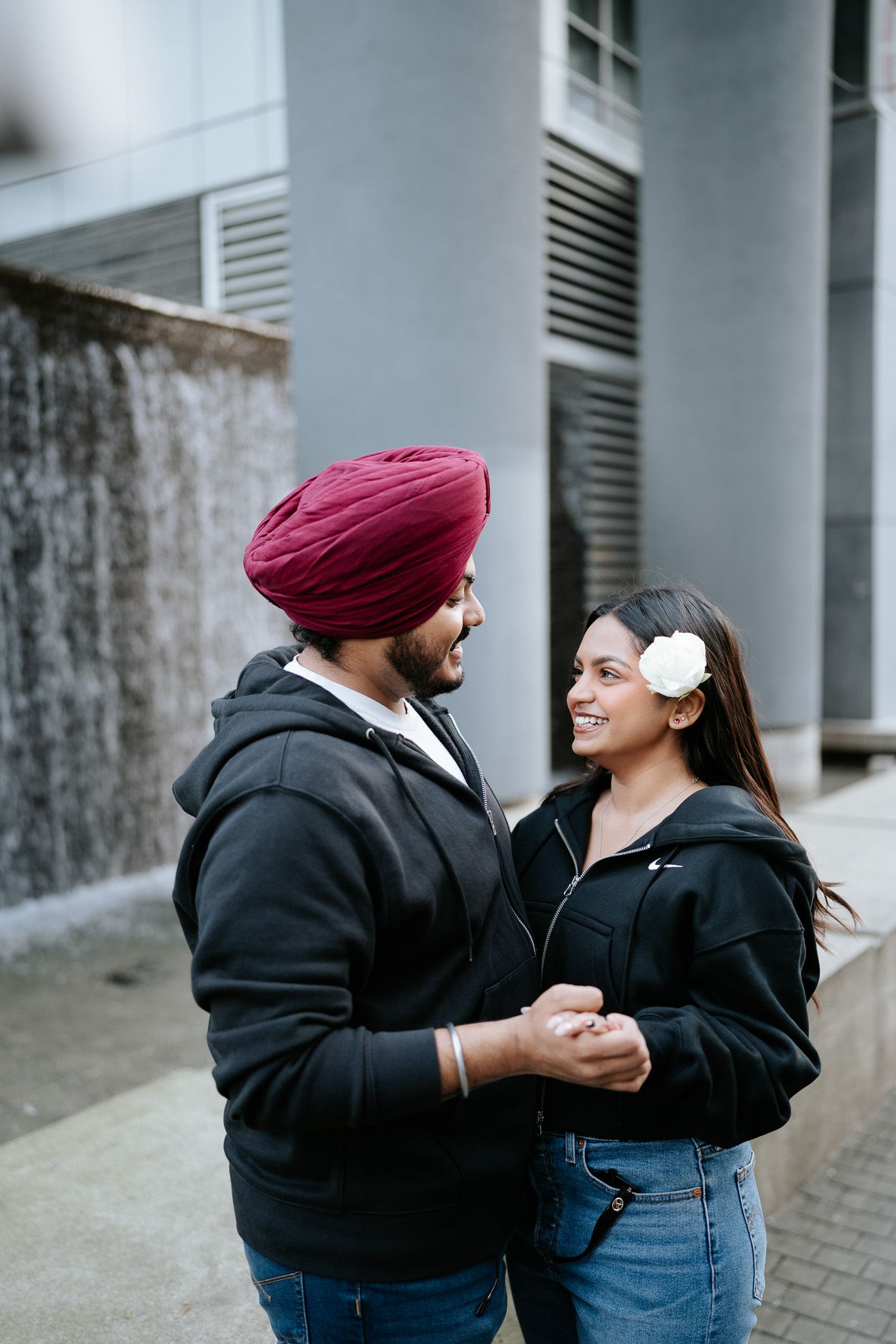 A couple wearing matching black hoodies share a romantic moment together on an urban street.