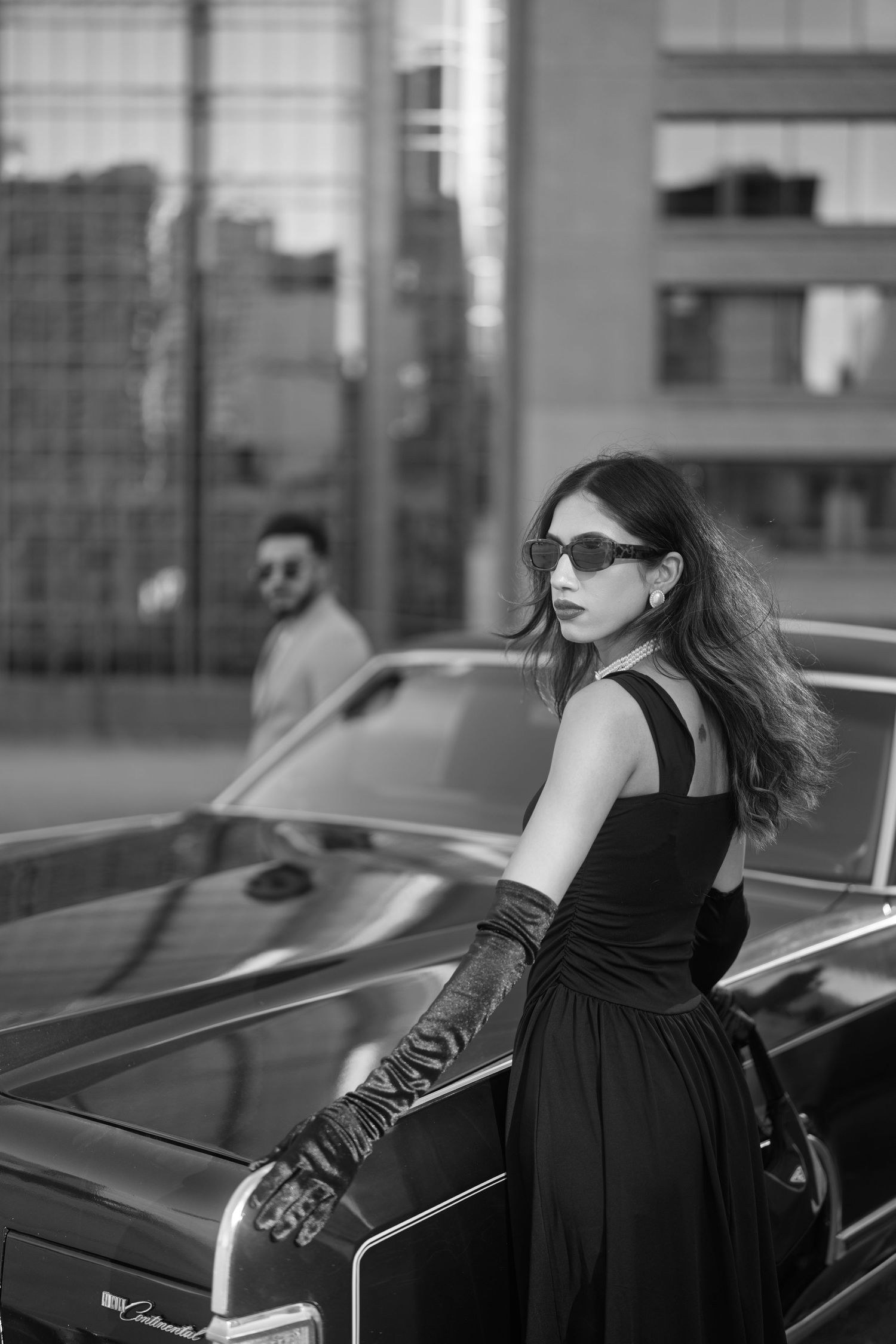 Black and white photo series of a person in a black dress posing elegantly against vintage cars.