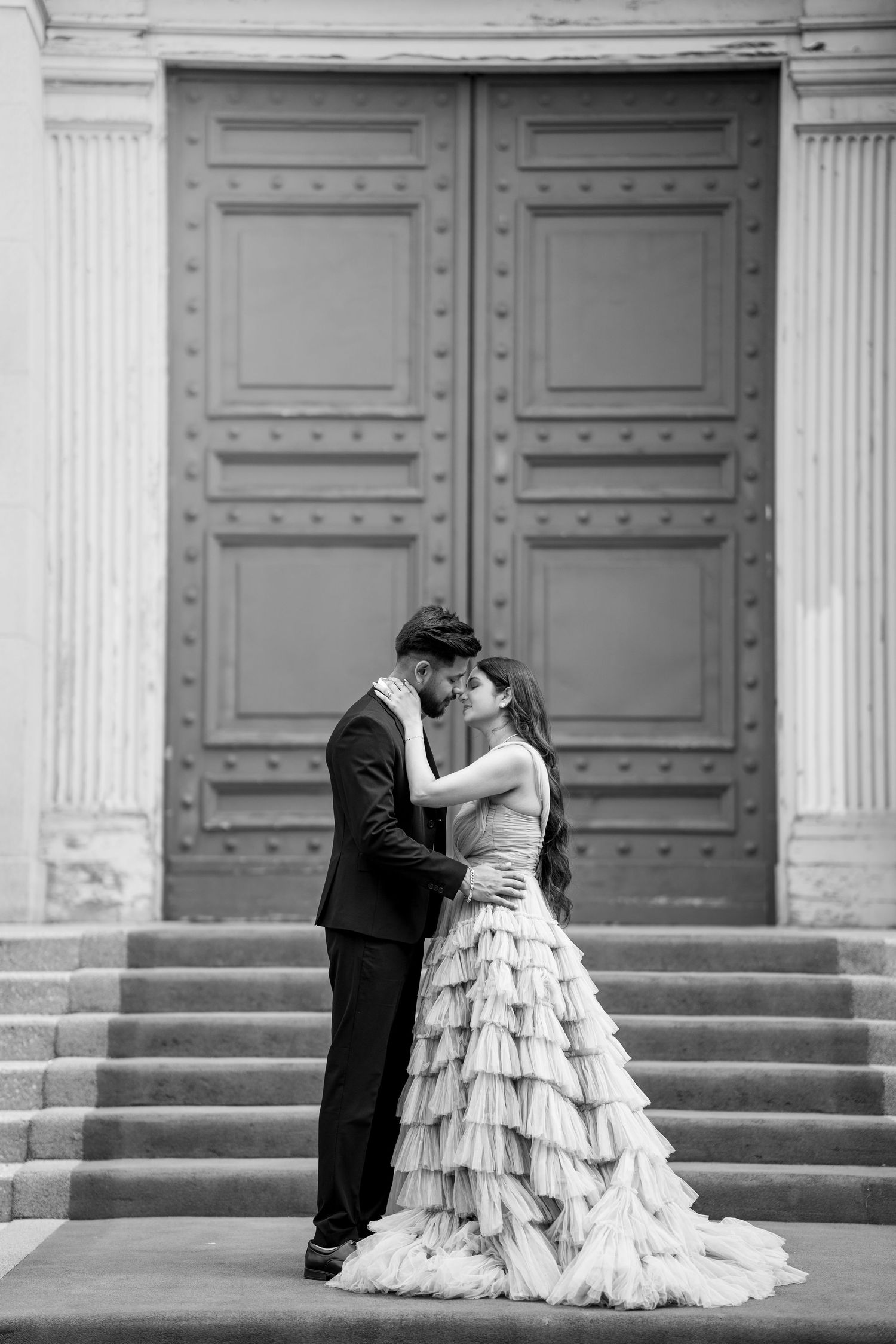 Wedding couple in formal attire pose romantically on grand stone steps.