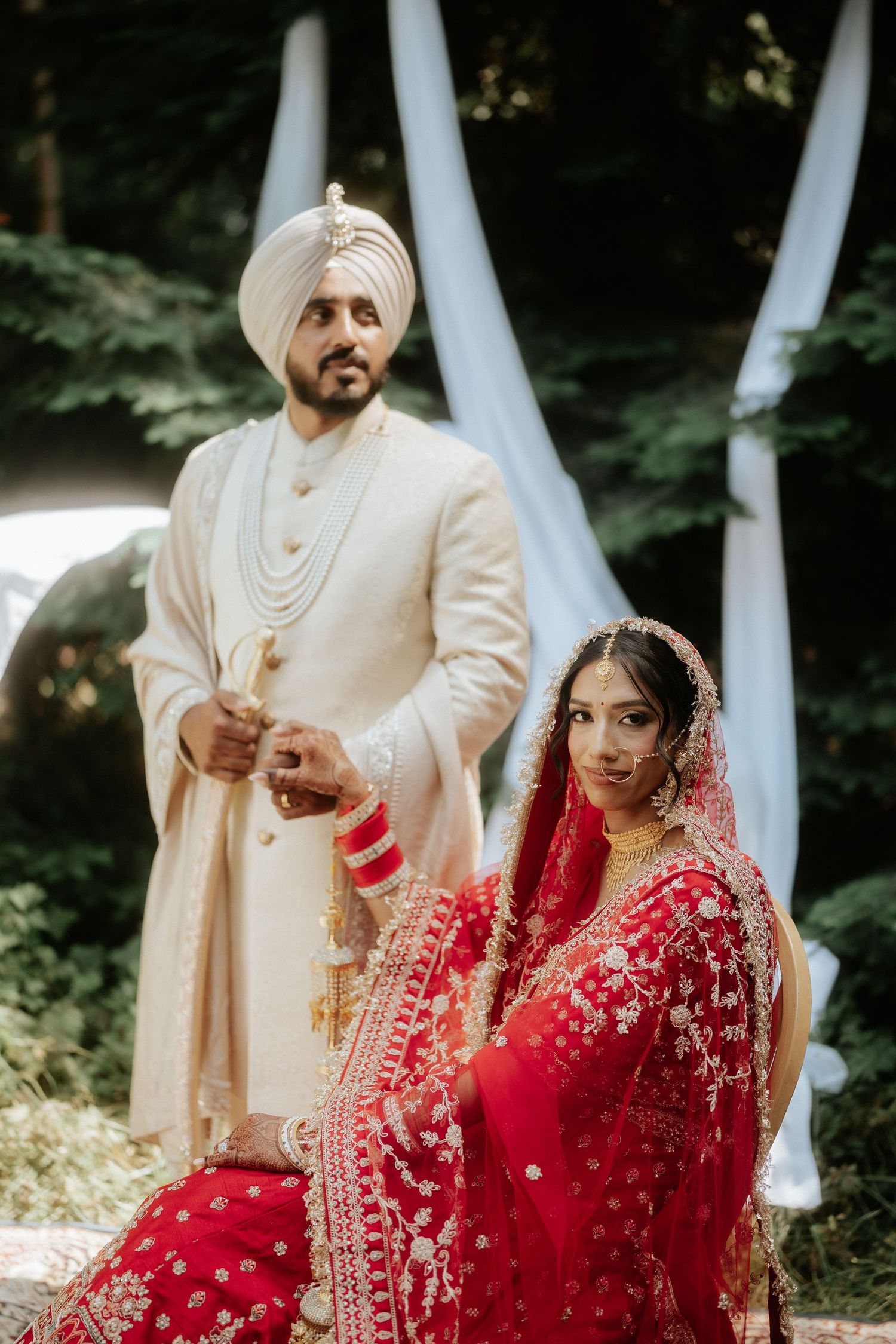 A bride in red and groom in white share candid moments during their Sikh wedding ceremony.