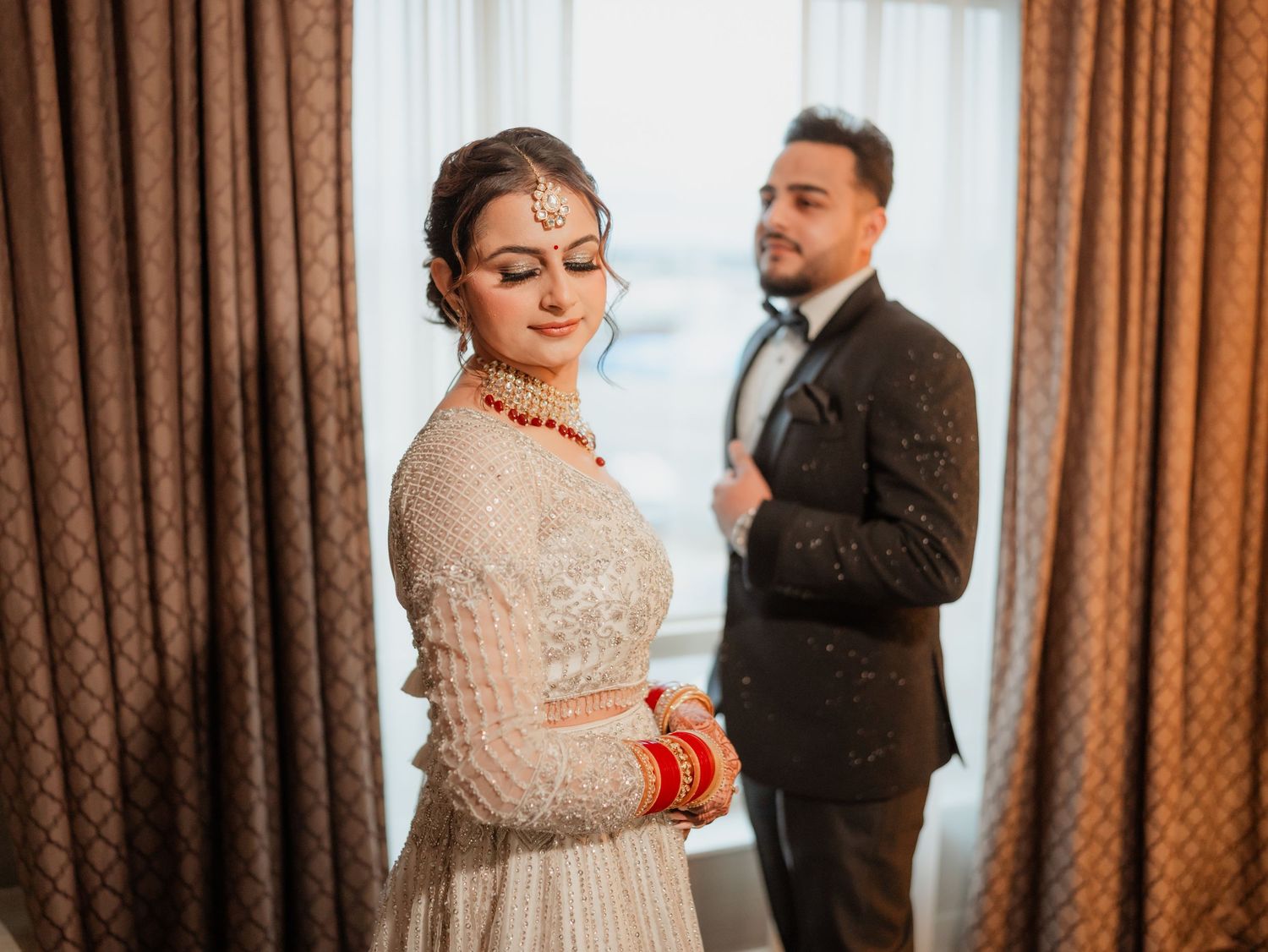 A couple shares a romantic moment in front of brown curtains during their wedding celebration.