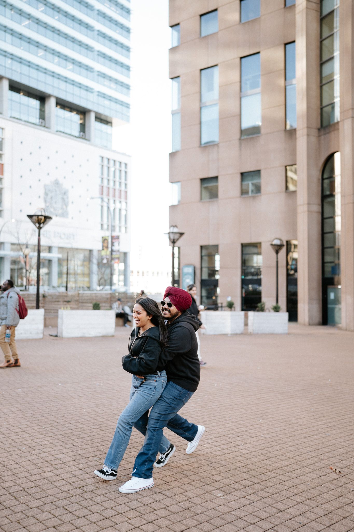 Person performing parkour moves on brick pavement in front of modern office buildings.