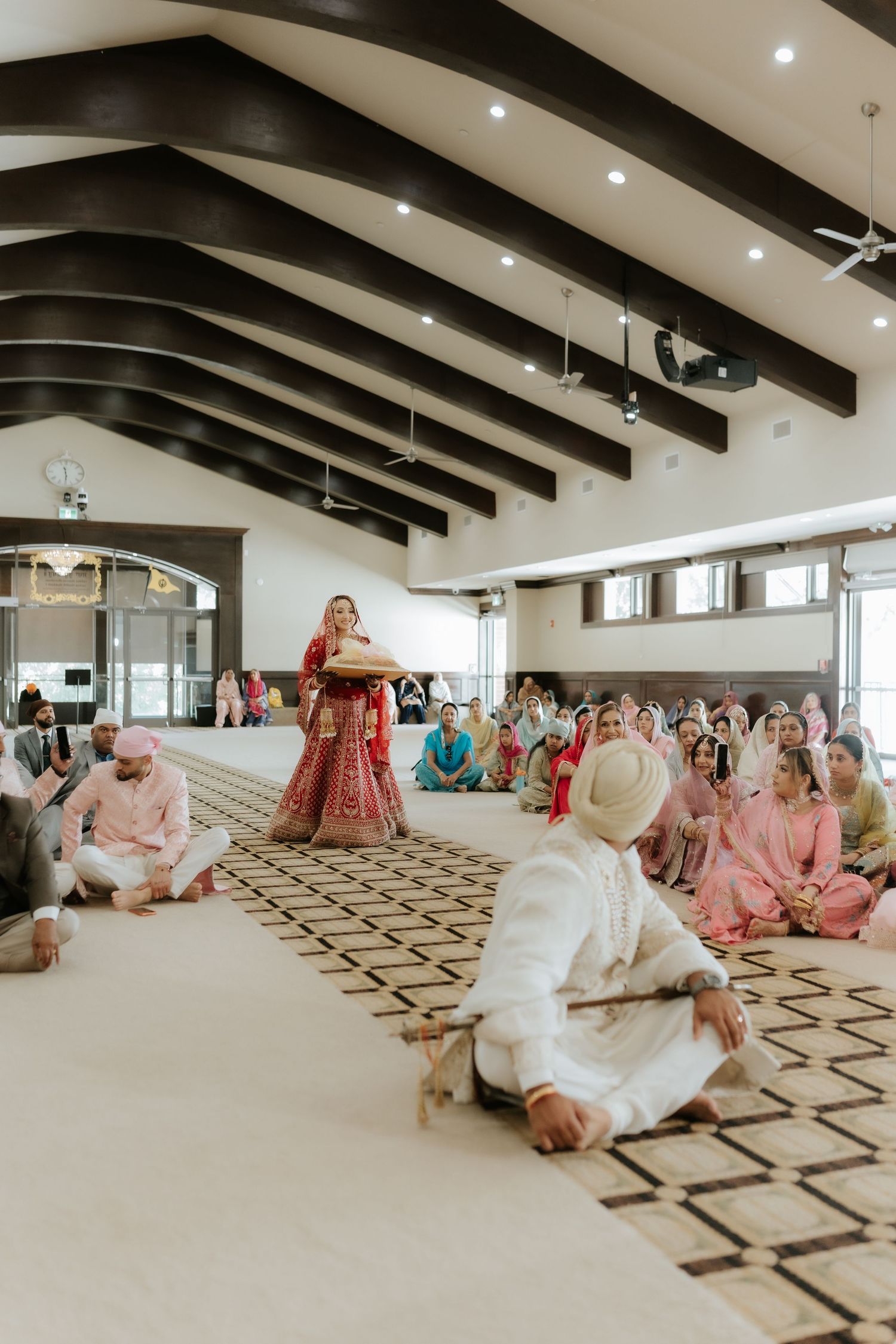 Sikh wedding ceremony with bride in red lehenga walking toward groom in white sherwani in elegant hall.