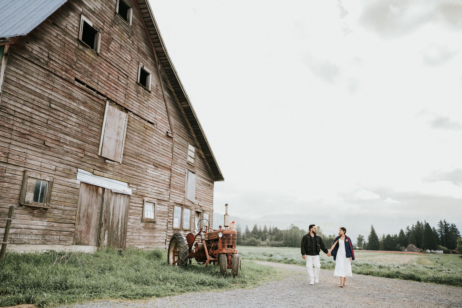 A rustic wooden barn stands weathered against a cloudy sky in a rural countryside setting.