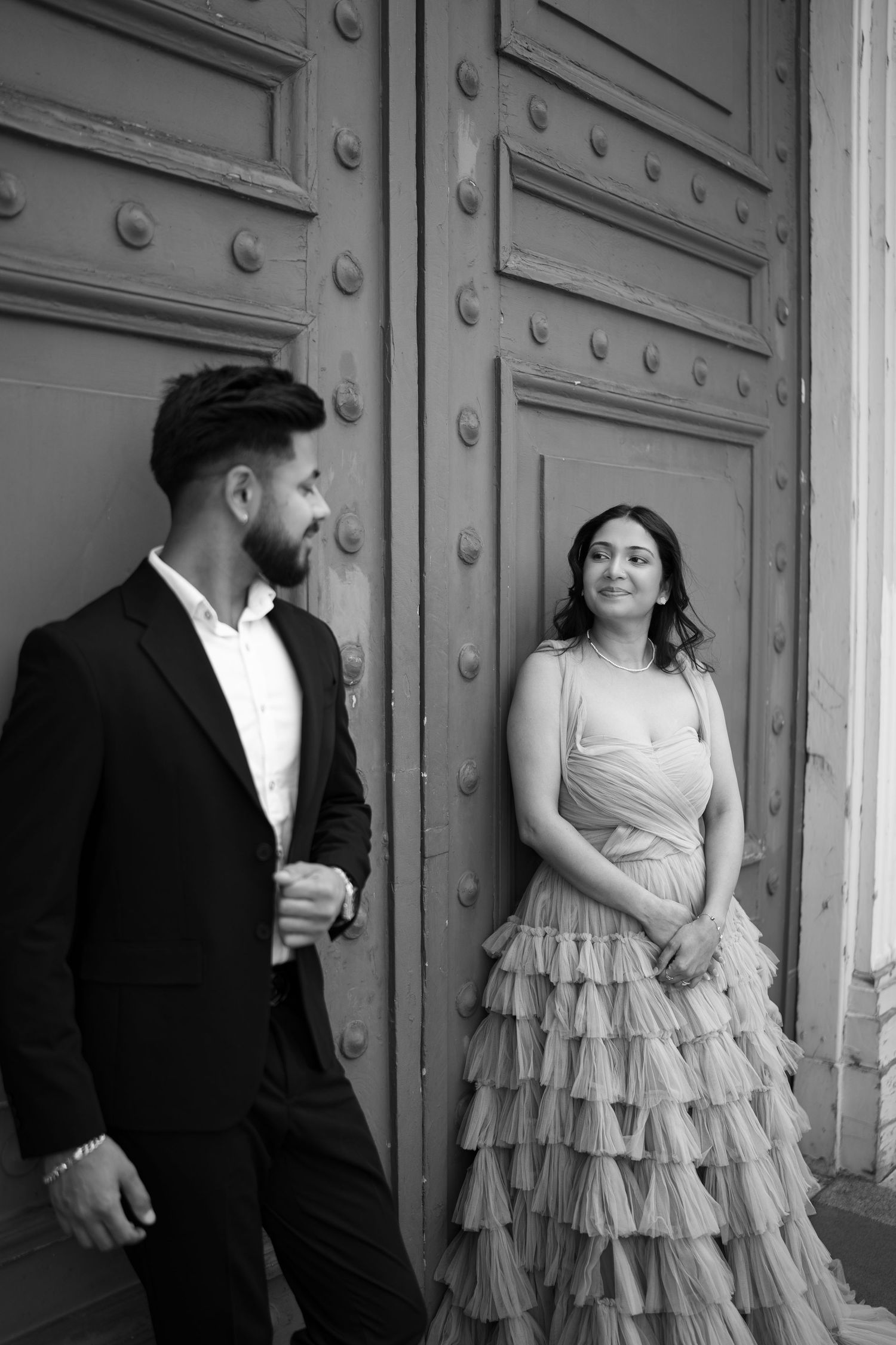 An elegant couple poses against vintage metal doors in formal attire.