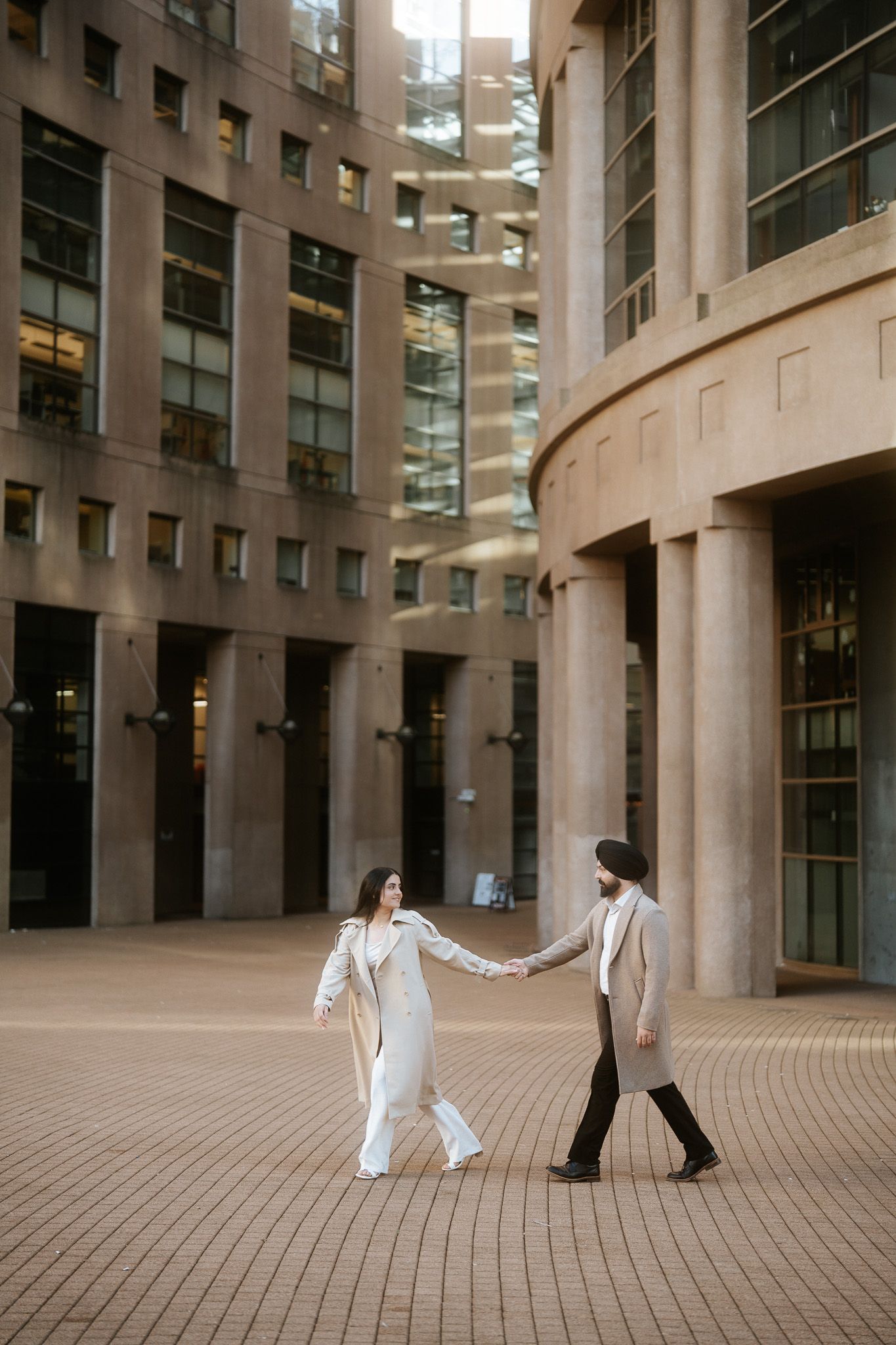 Couple in white outfits dancing gracefully in a modern architectural courtyard with tall columns and glass windows.