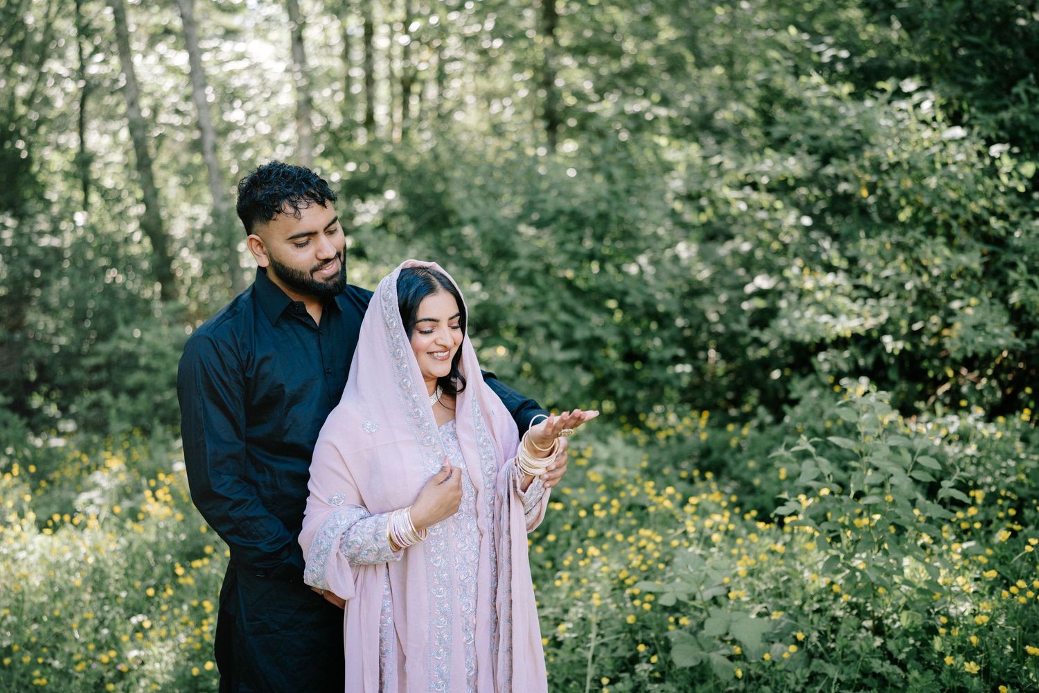 Couple poses together in a lush garden setting with blooming yellow flowers and greenery.