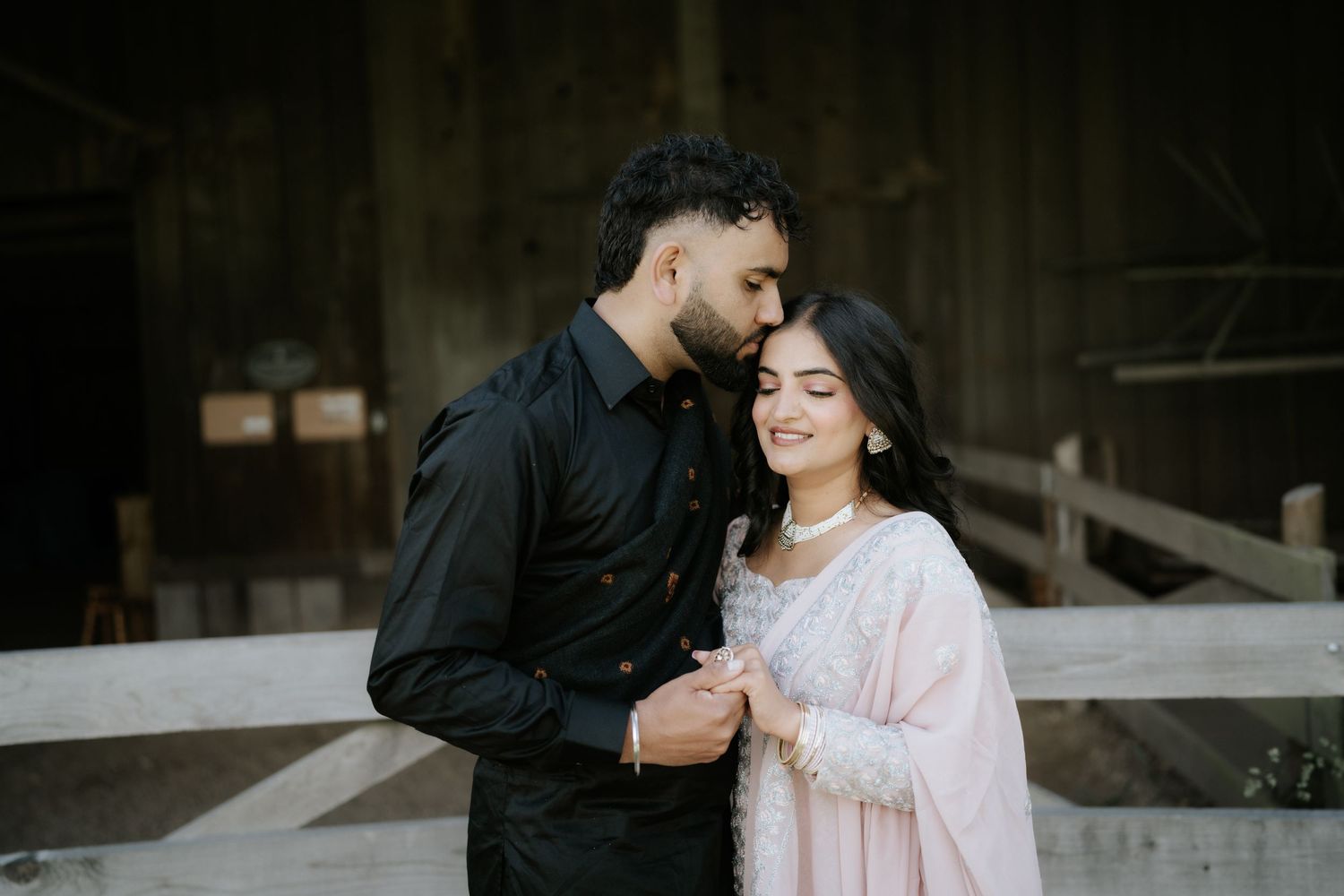 A couple shares intimate moments in front of a rustic barn setting.