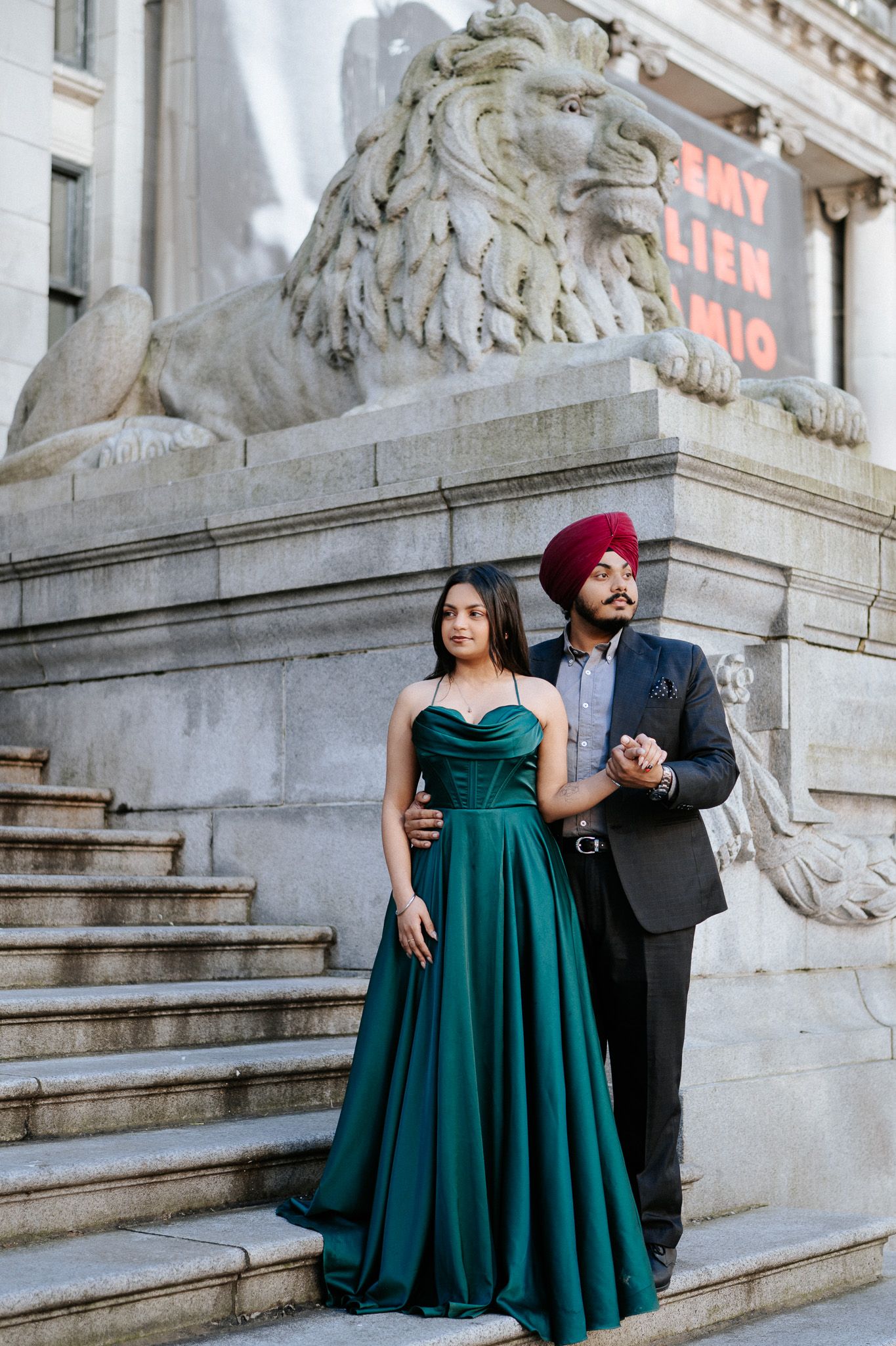 A couple in formal attire poses elegantly on stone steps, with the person in a green gown and another in a dark suit.