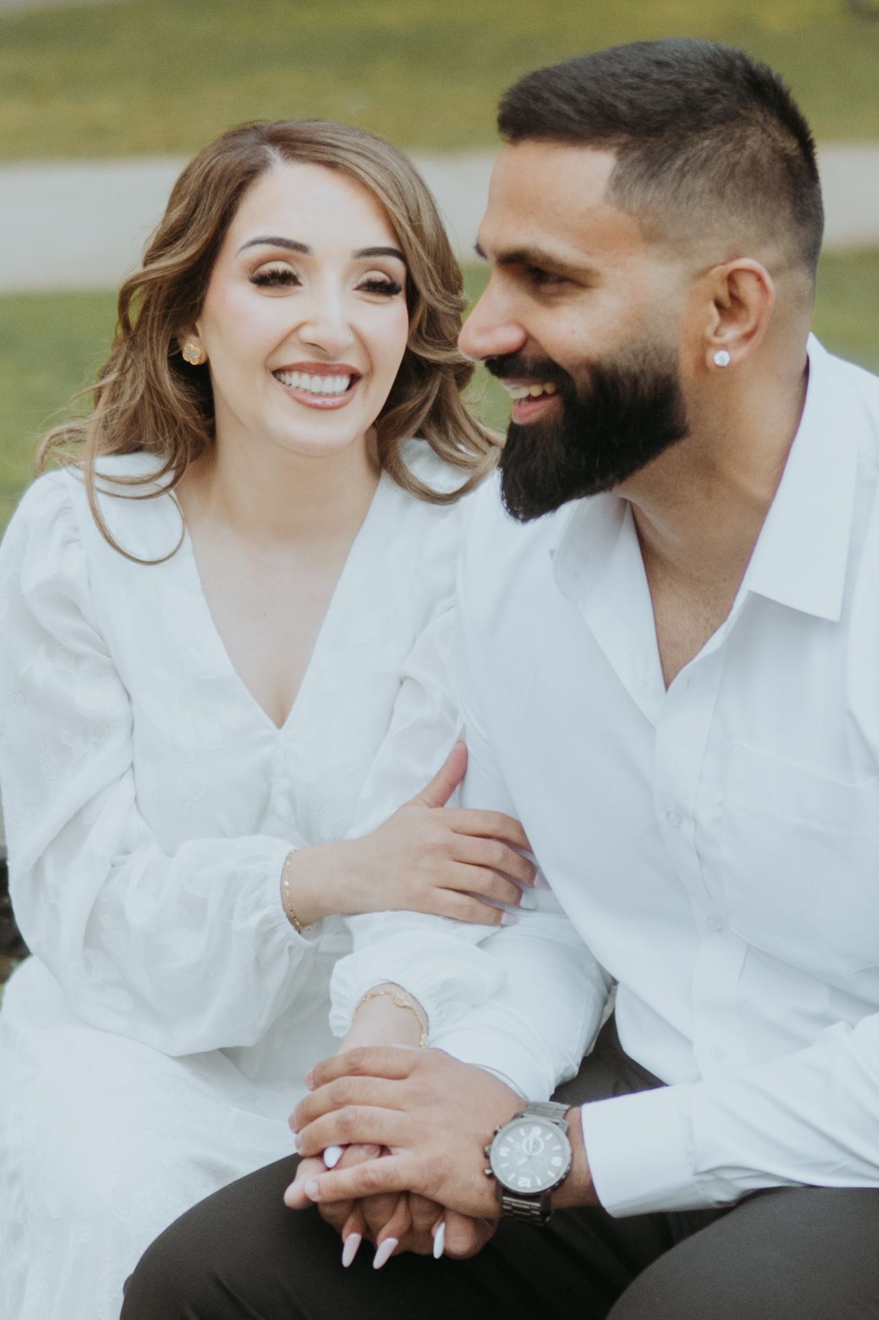 Two people in matching white shirts share joyful laughter while sitting close together outdoors.