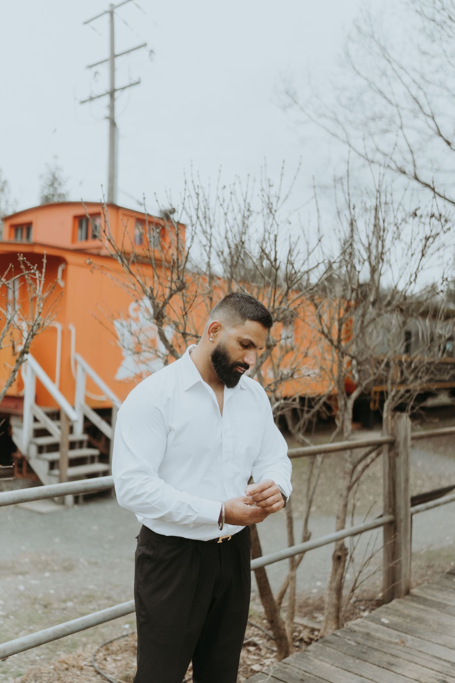 Person in classic white and black attire poses near orange train car and wooden fence.