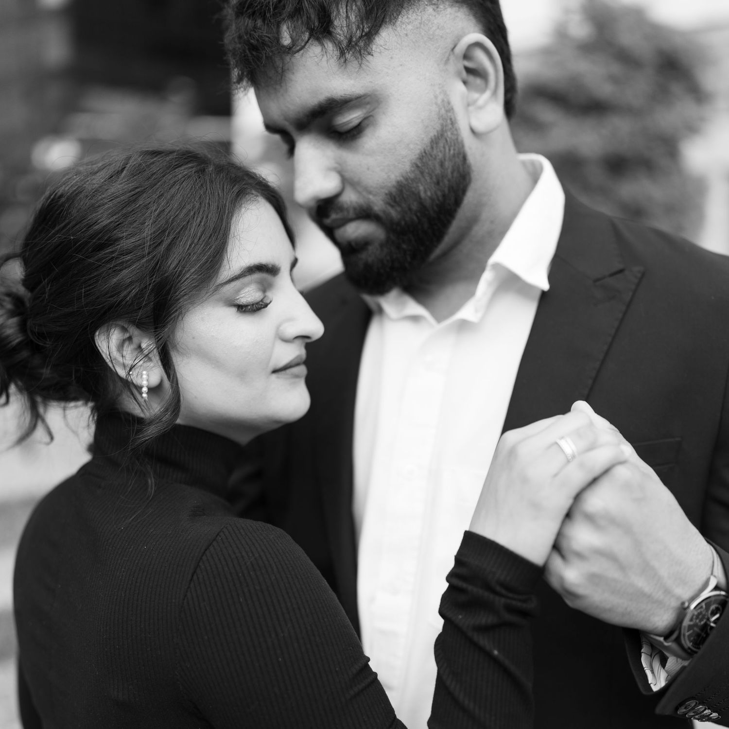 A romantic black and white portrait of a couple in formal wear sharing an intimate moment.
