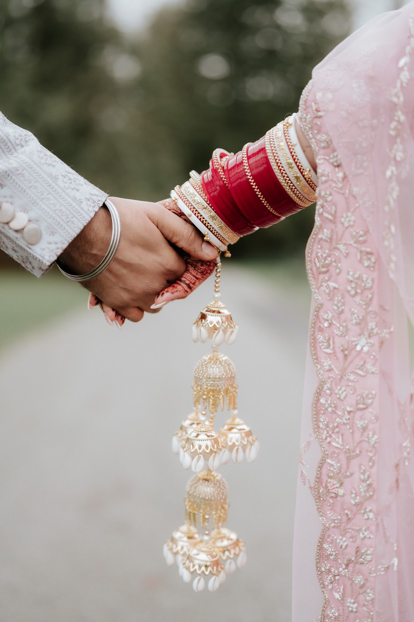 Close-up of hands wearing traditional Indian wedding bangles holding ornate gold and pearl kalire jewelry.