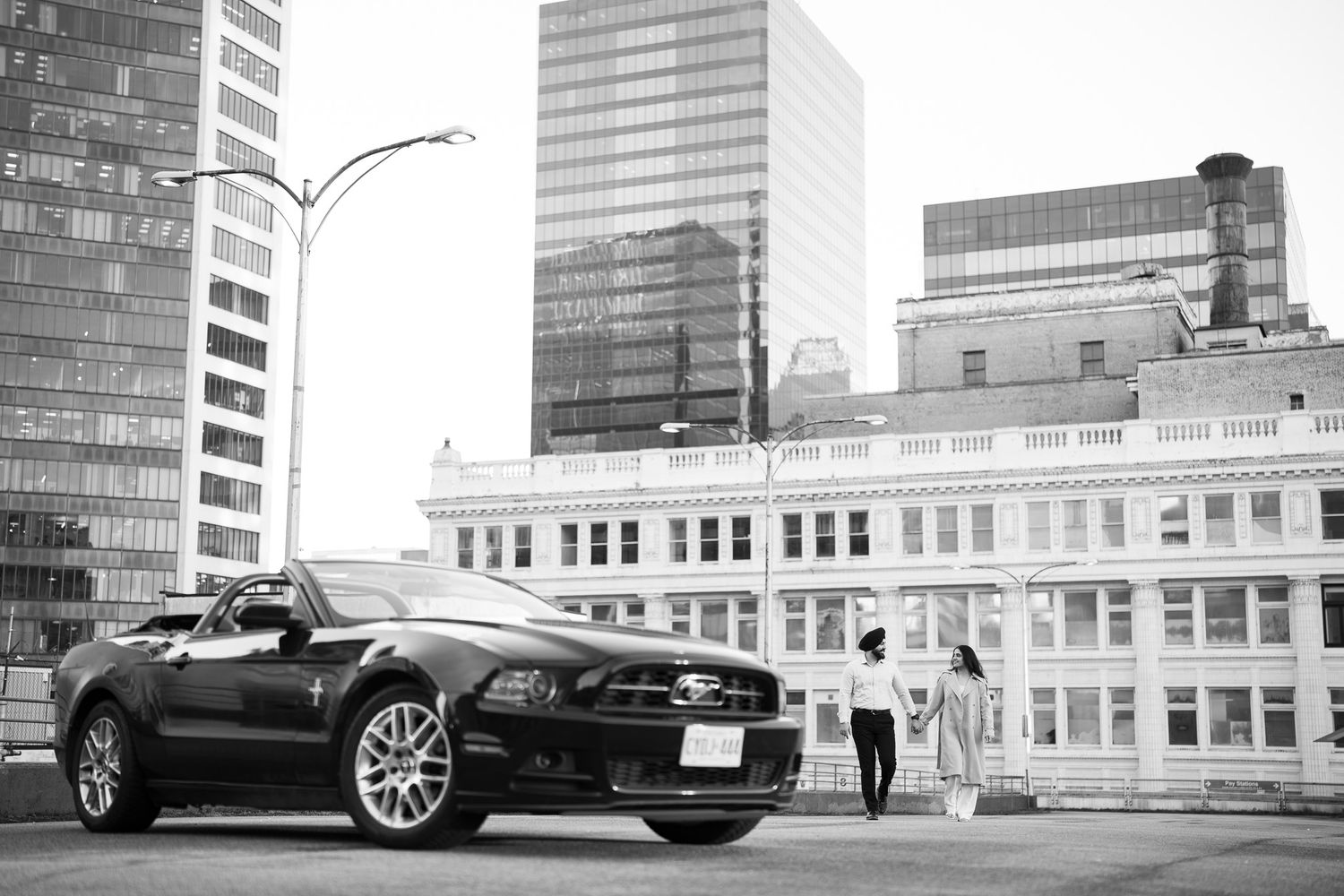 A black Ford Mustang convertible parked on a city street with modern office buildings in the background.