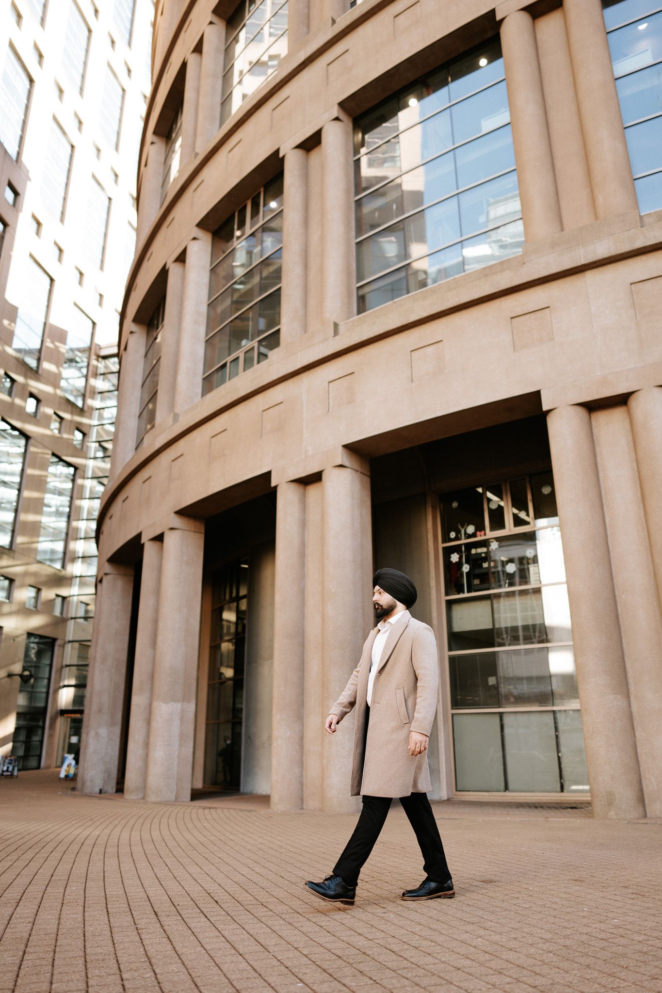 Person in a light coat walks along curved architectural columns of a modern building exterior.