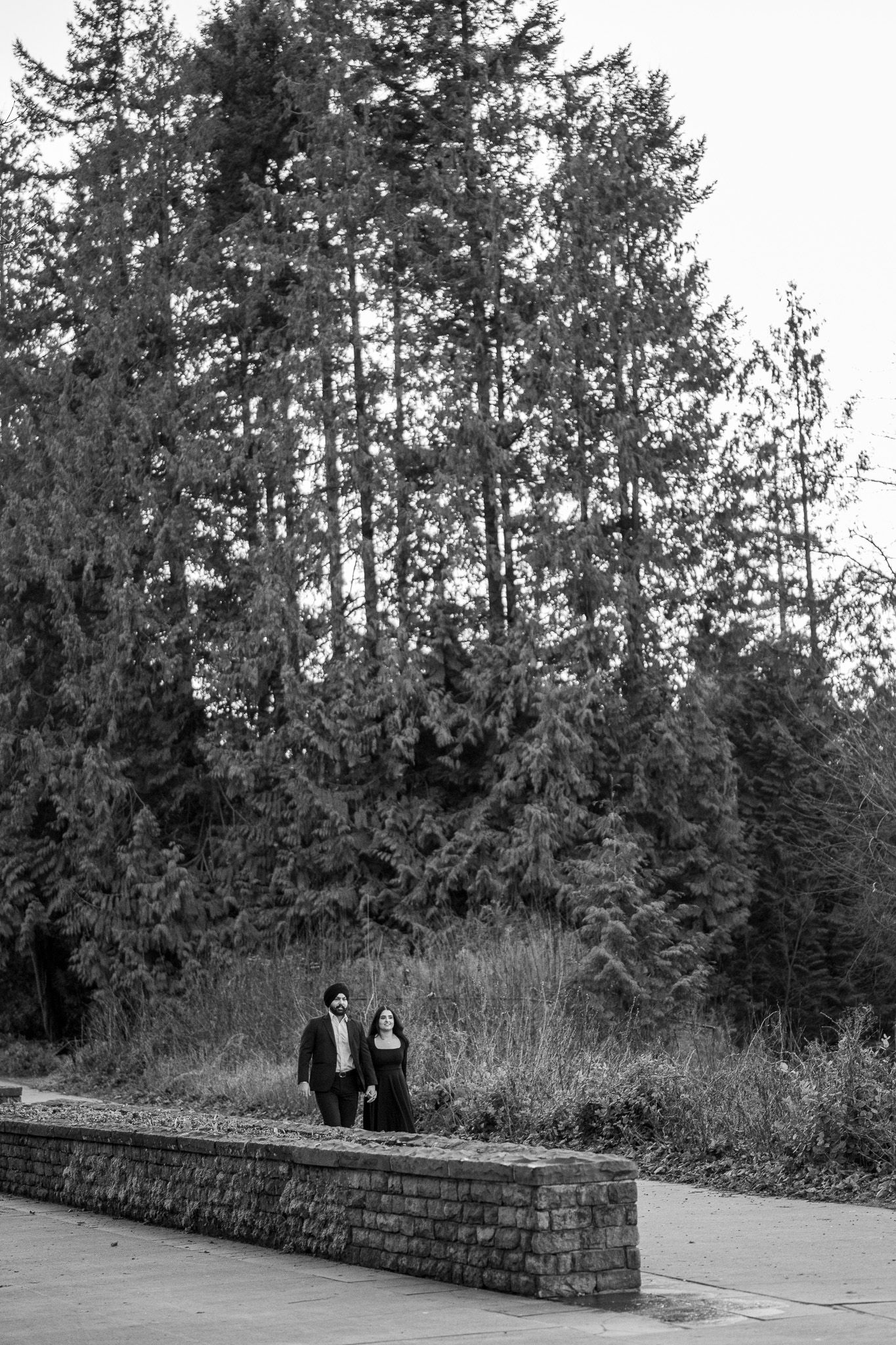 A sequence of black and white photos shows two figures sitting on a stone wall with evergreen trees in the background.