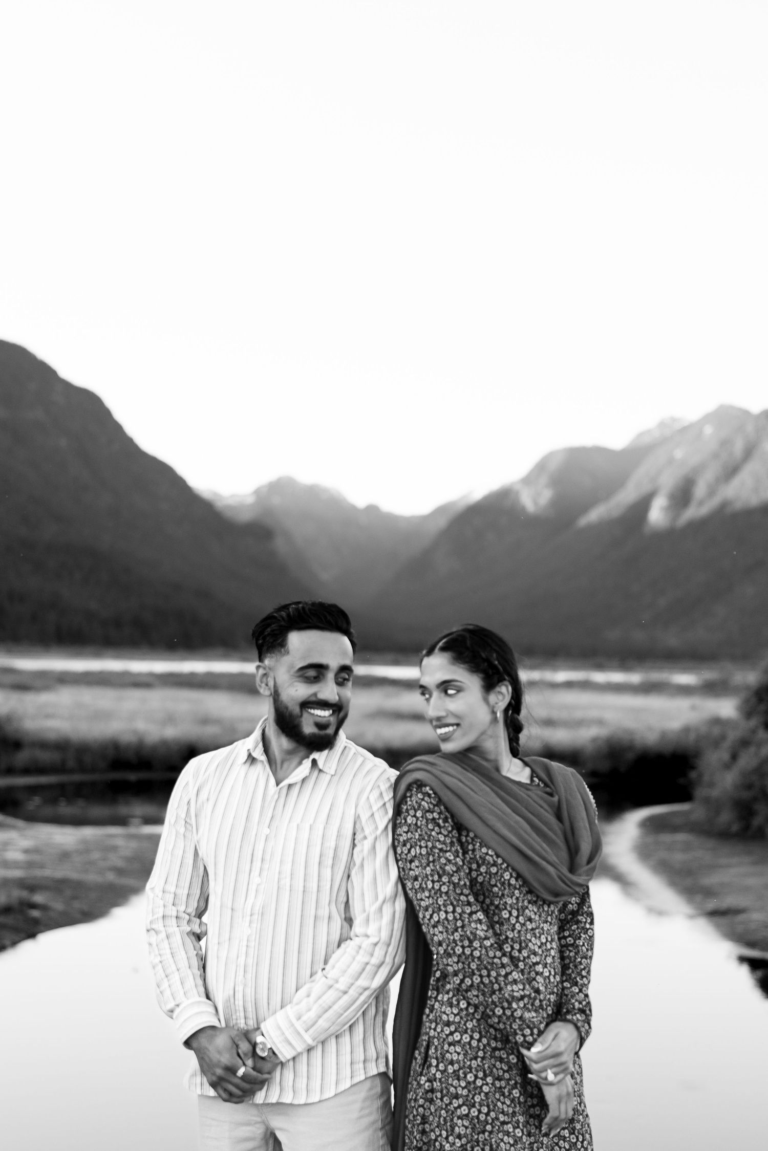 A couple shares joyful moments together against a scenic mountain landscape with a serene lake in the background.