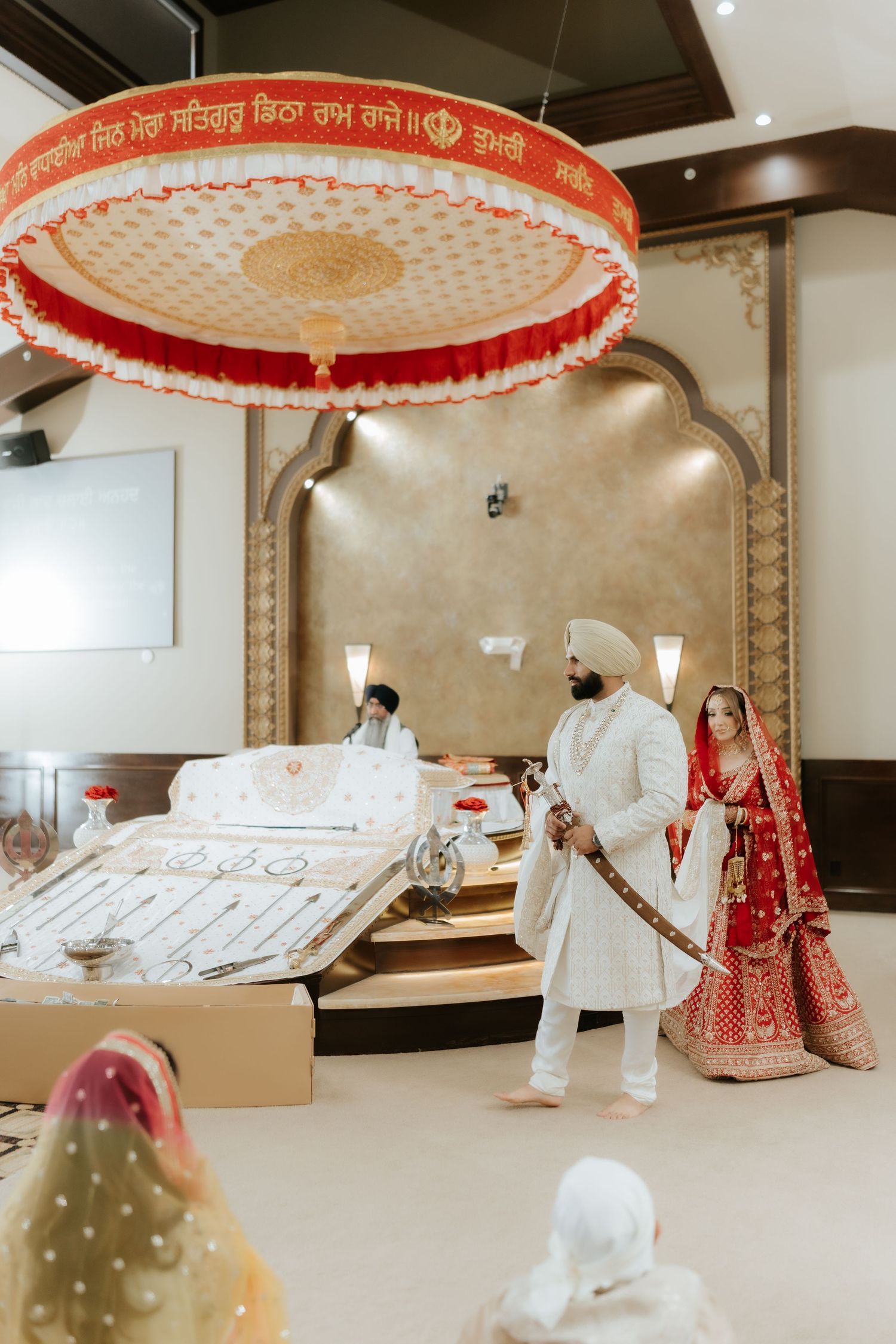 Sikh wedding couple in traditional attire performing Anand Karaj ceremony at Gurdwara, bride in red lehenga.