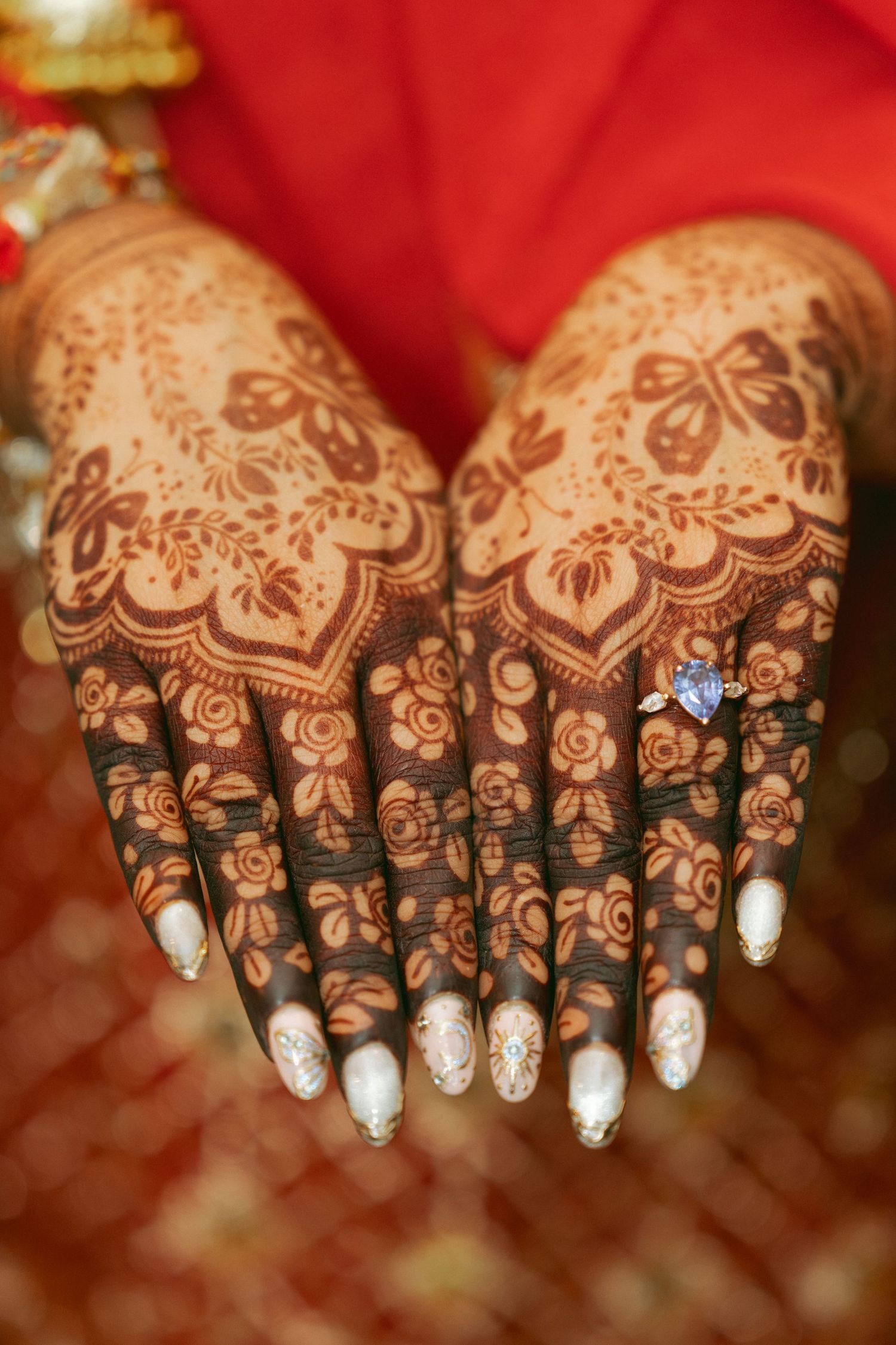 Close-up of bride's hands adorned with intricate henna mehndi designs and a blue gemstone ring.
