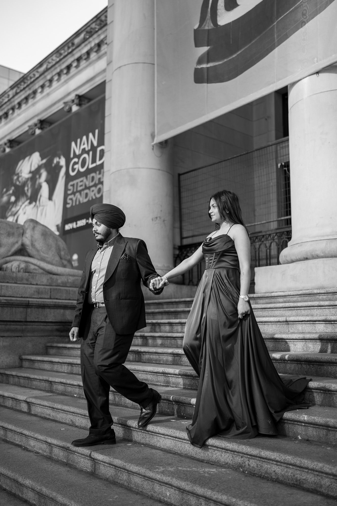 Sequence of black and white photos showing a couple playfully walking up stone steps outside a building.