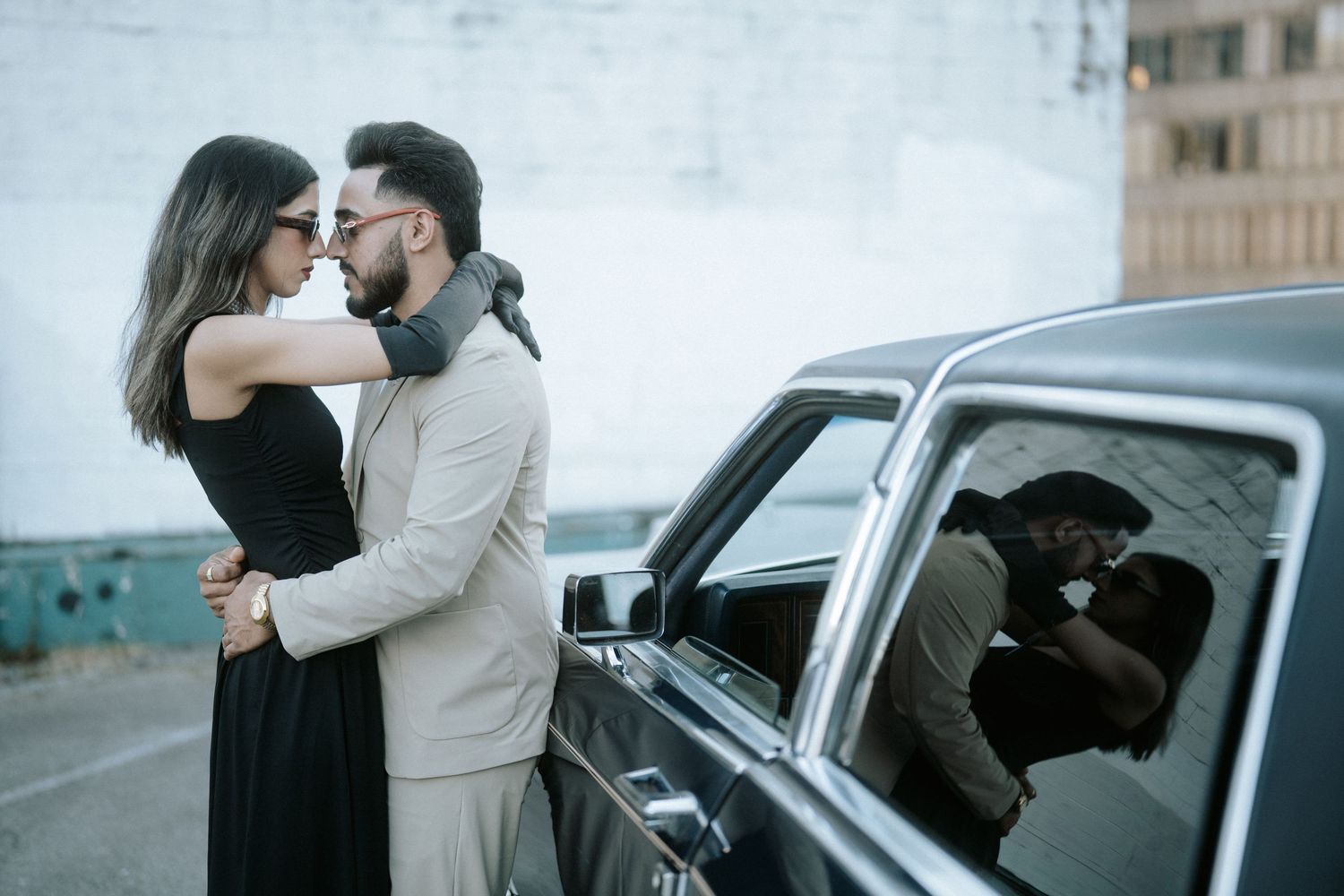 A couple embraces in a romantic kiss beside a car on a city street.
