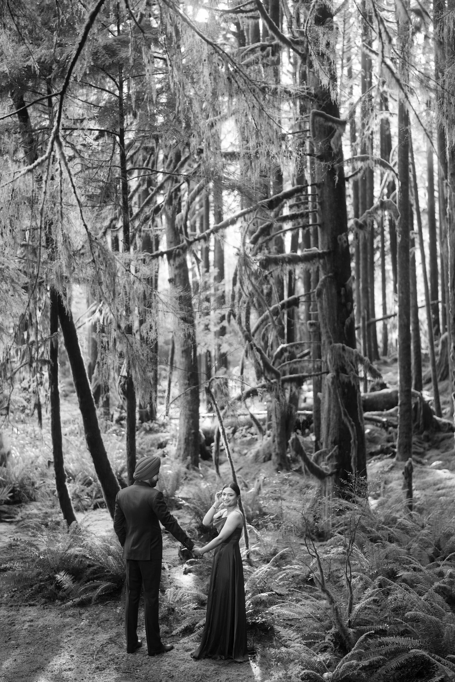 Black and white photo series of a couple standing among towering trees in a forest.