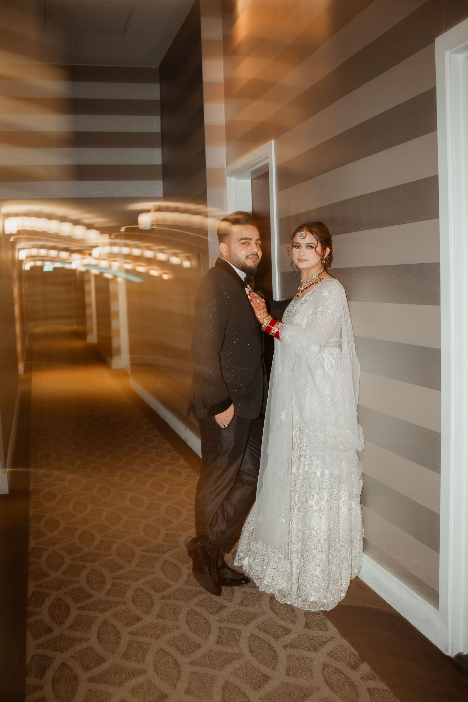 A couple shares a tender moment while walking down a carpeted hallway.