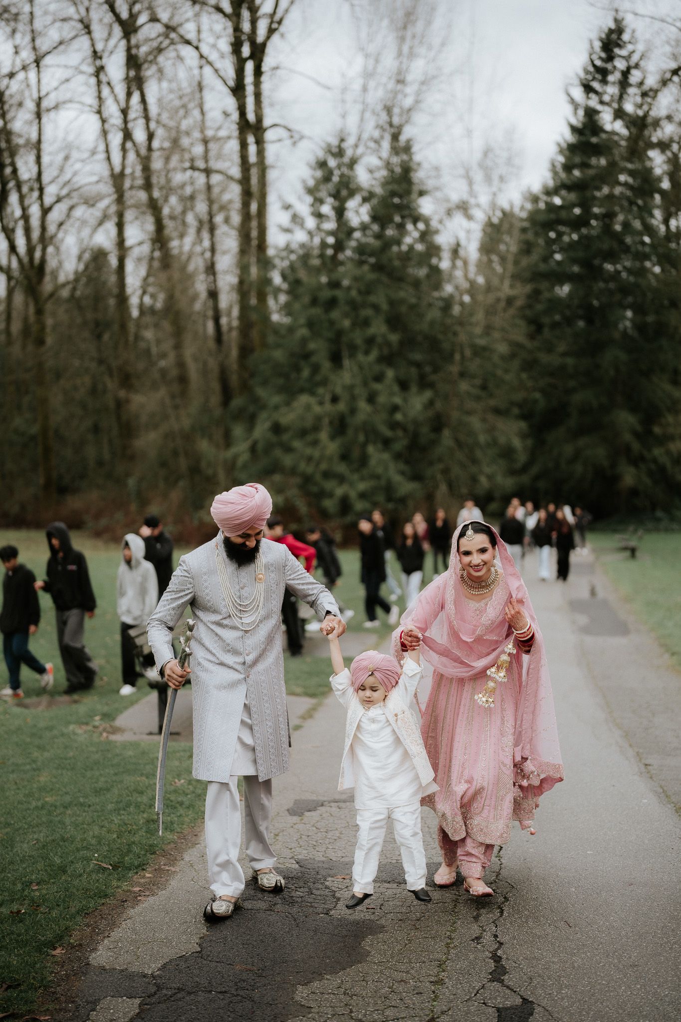 A family walks together on a path through a park wearing coordinated white and pink traditional South Asian attire.