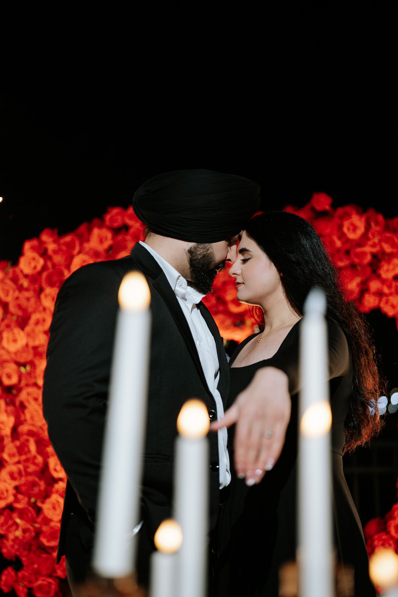 A romantic silhouette of a couple embracing against a backdrop of glowing red roses and candlelight.