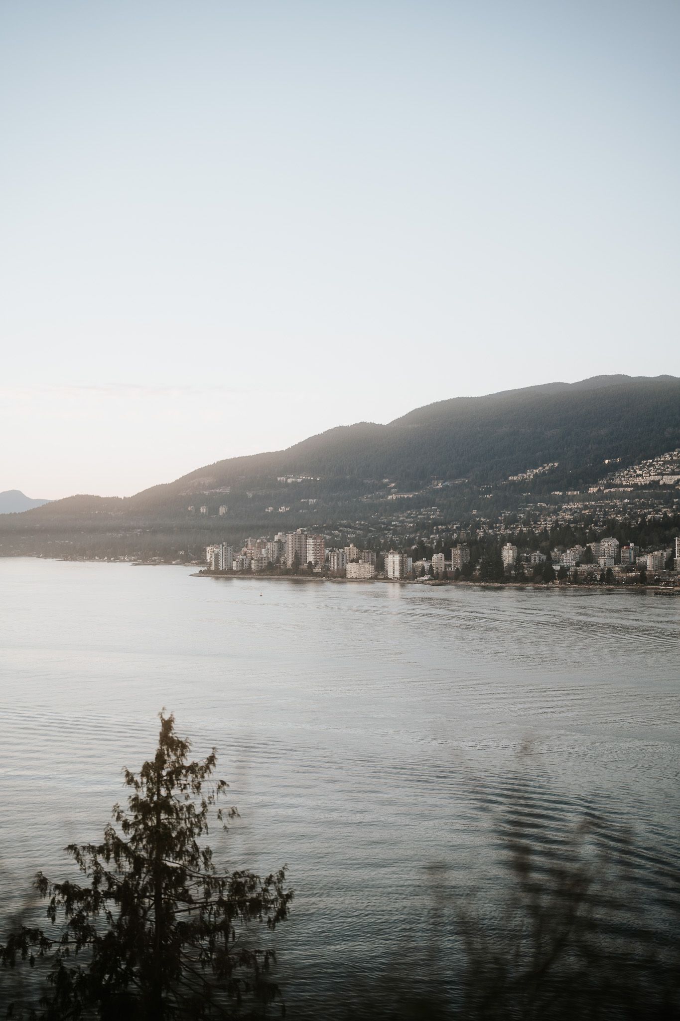 A panoramic view of Vancouver's cityscape along the waterfront with mountains in the background at dusk.