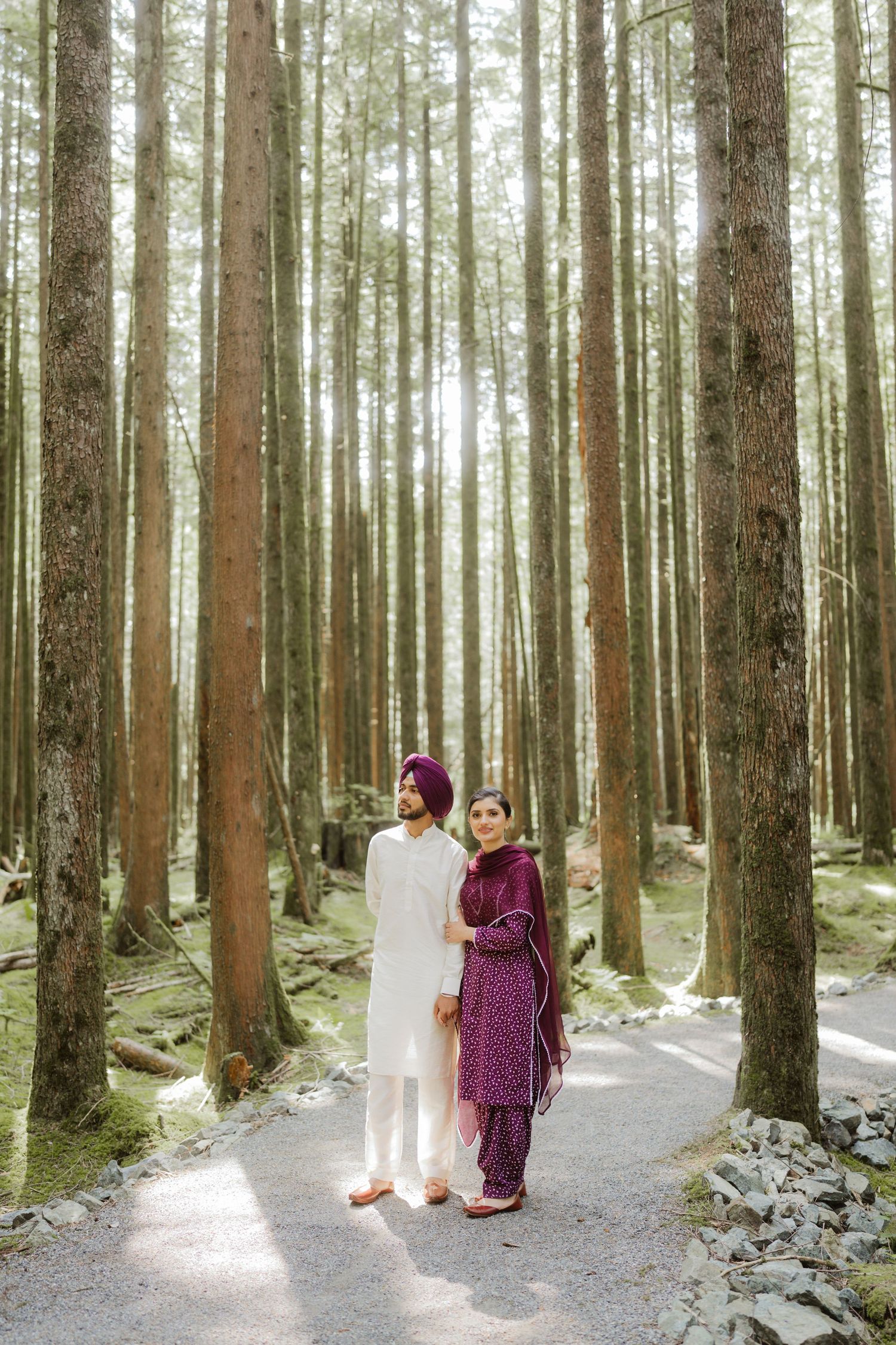 Sikh couple standing on a forest path, man in white kurta with purple turban, woman in purple salwar kameez.