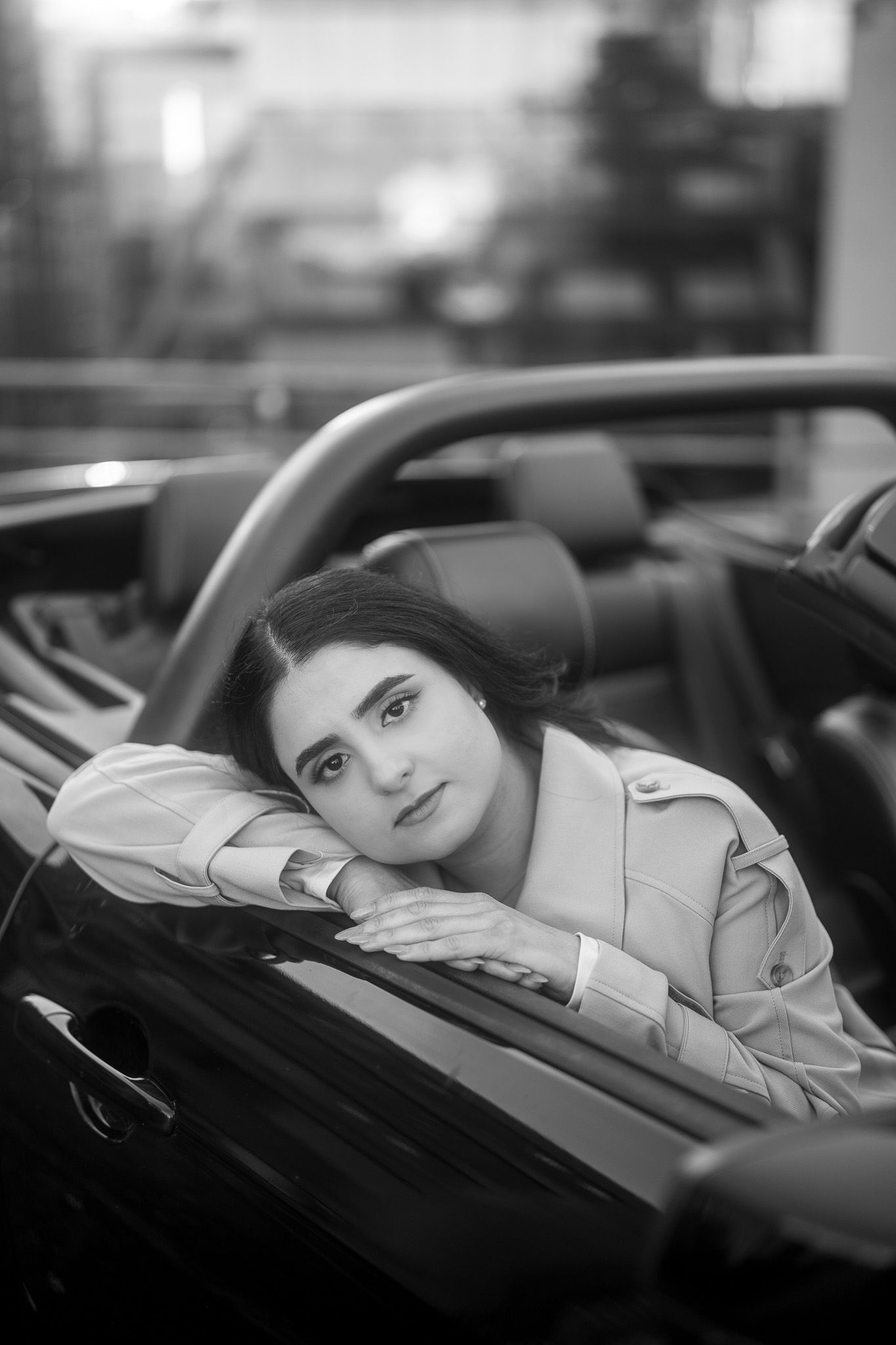 Black and white portrait of someone resting their head on the door of a luxury convertible car.