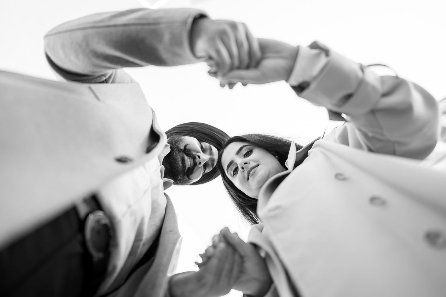 Black and white low angle view of three people huddling together in a circle formation.