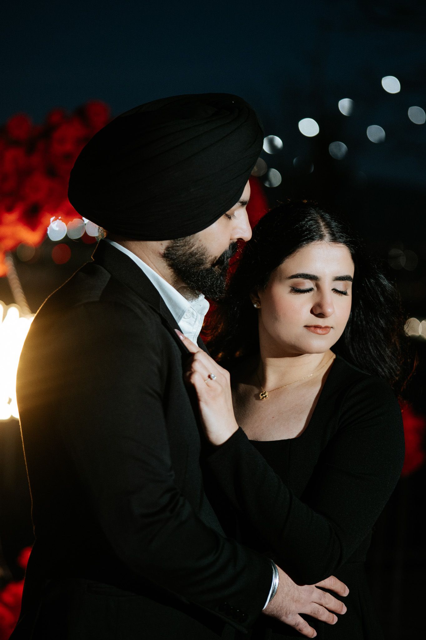 A romantic couple in formal attire shares an intimate moment against a dark background with bokeh lights.