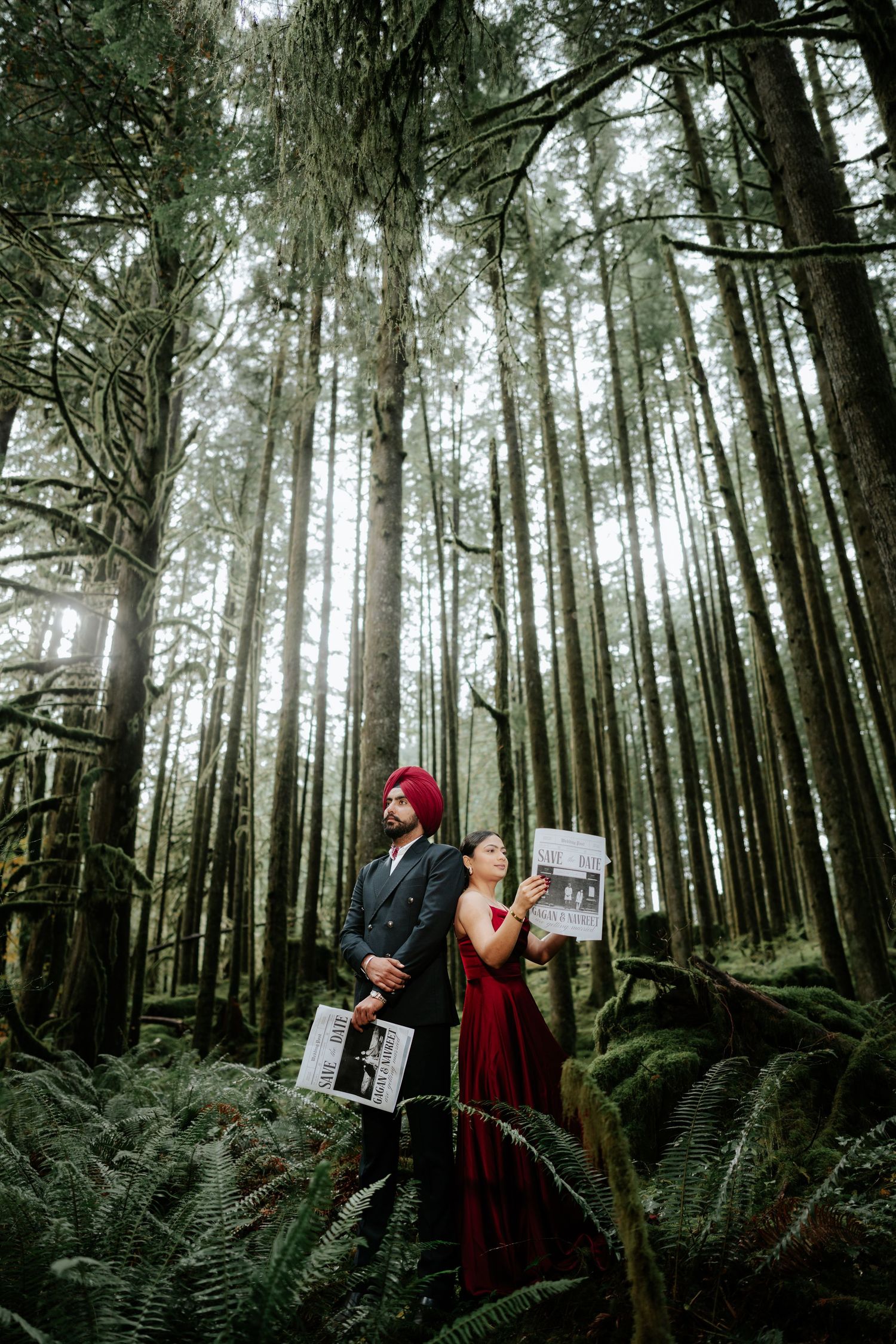 A couple poses back-to-back with newspapers in a majestic forest of tall trees.