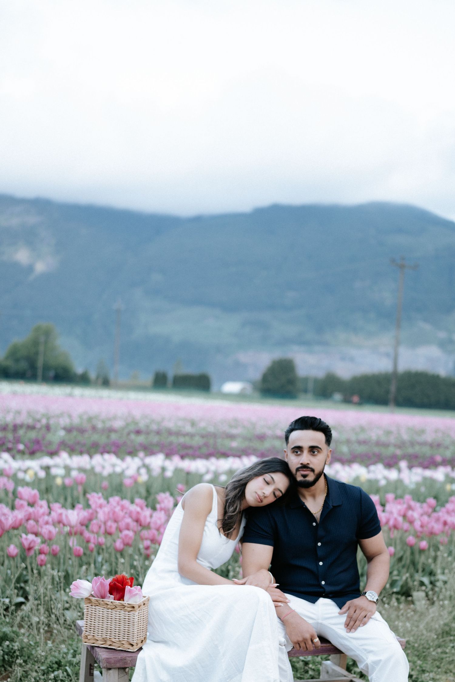 A couple relaxes together in a scenic tulip field with mountains in the background.