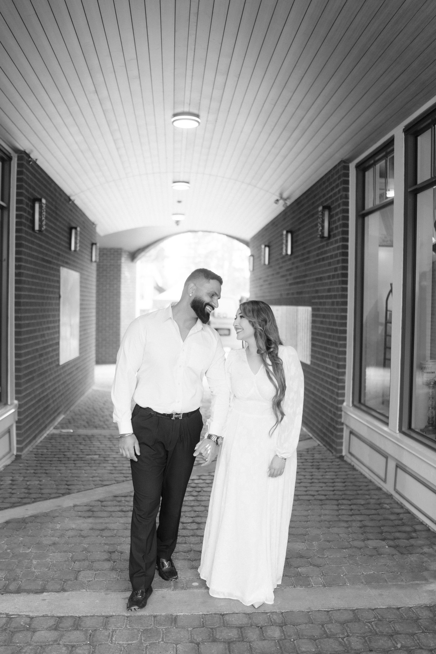 A couple walks down a brick-lined hallway in formal attire creating a romantic silhouette.