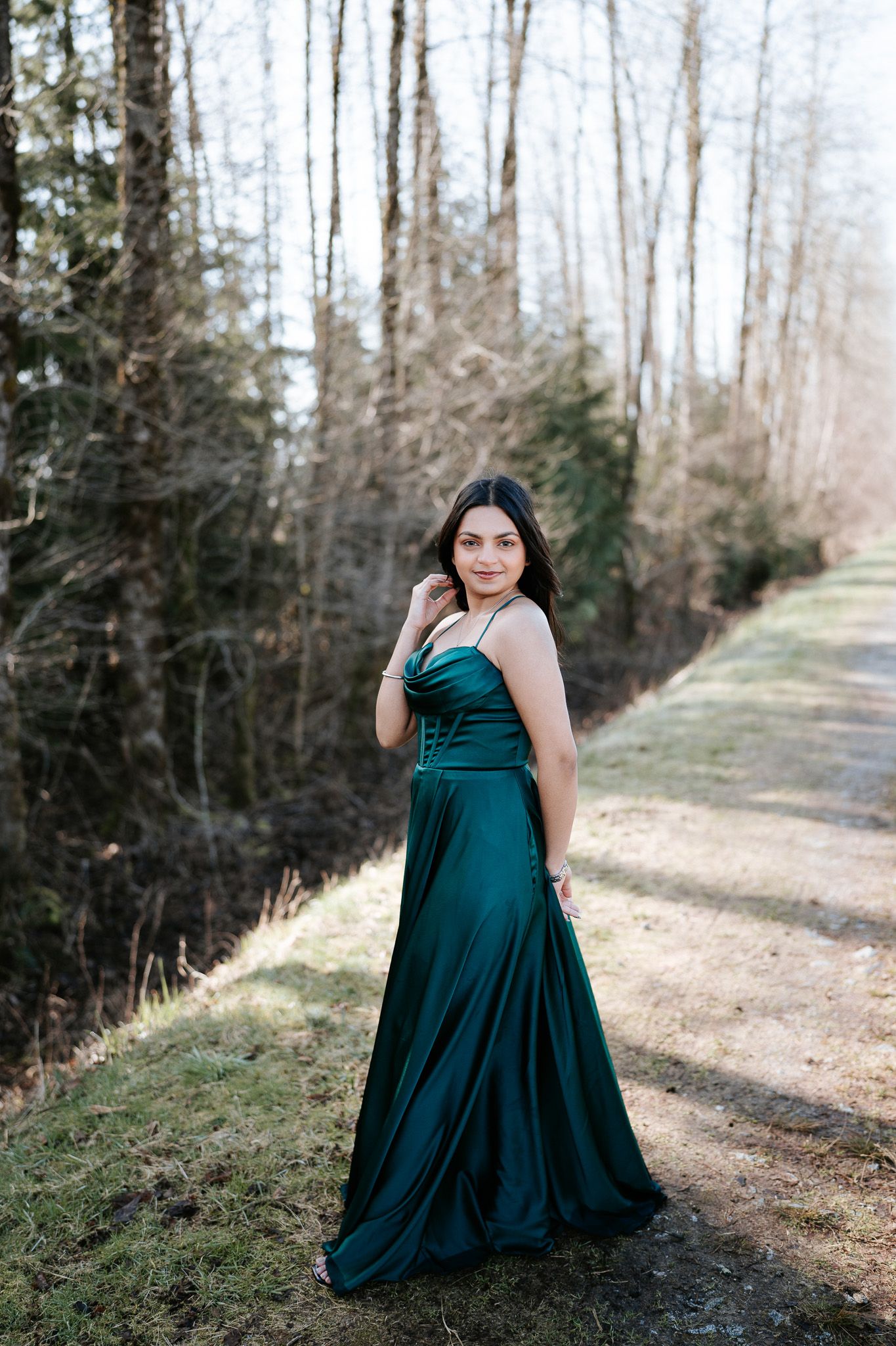 A person in an elegant emerald green gown poses gracefully on a wooded path during a photo session.