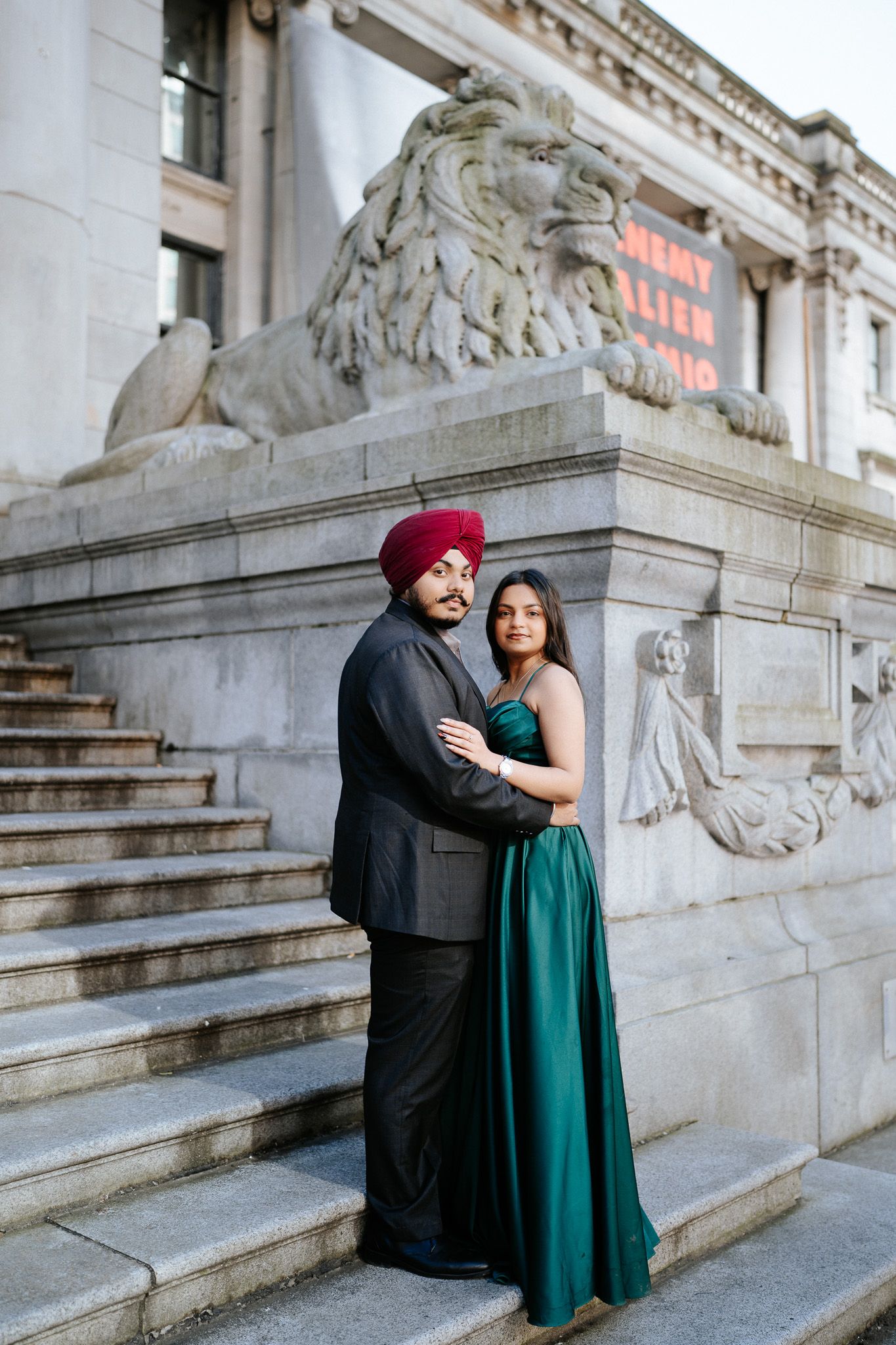 A couple embraces on stone steps outside a historic building with ornate architectural details.