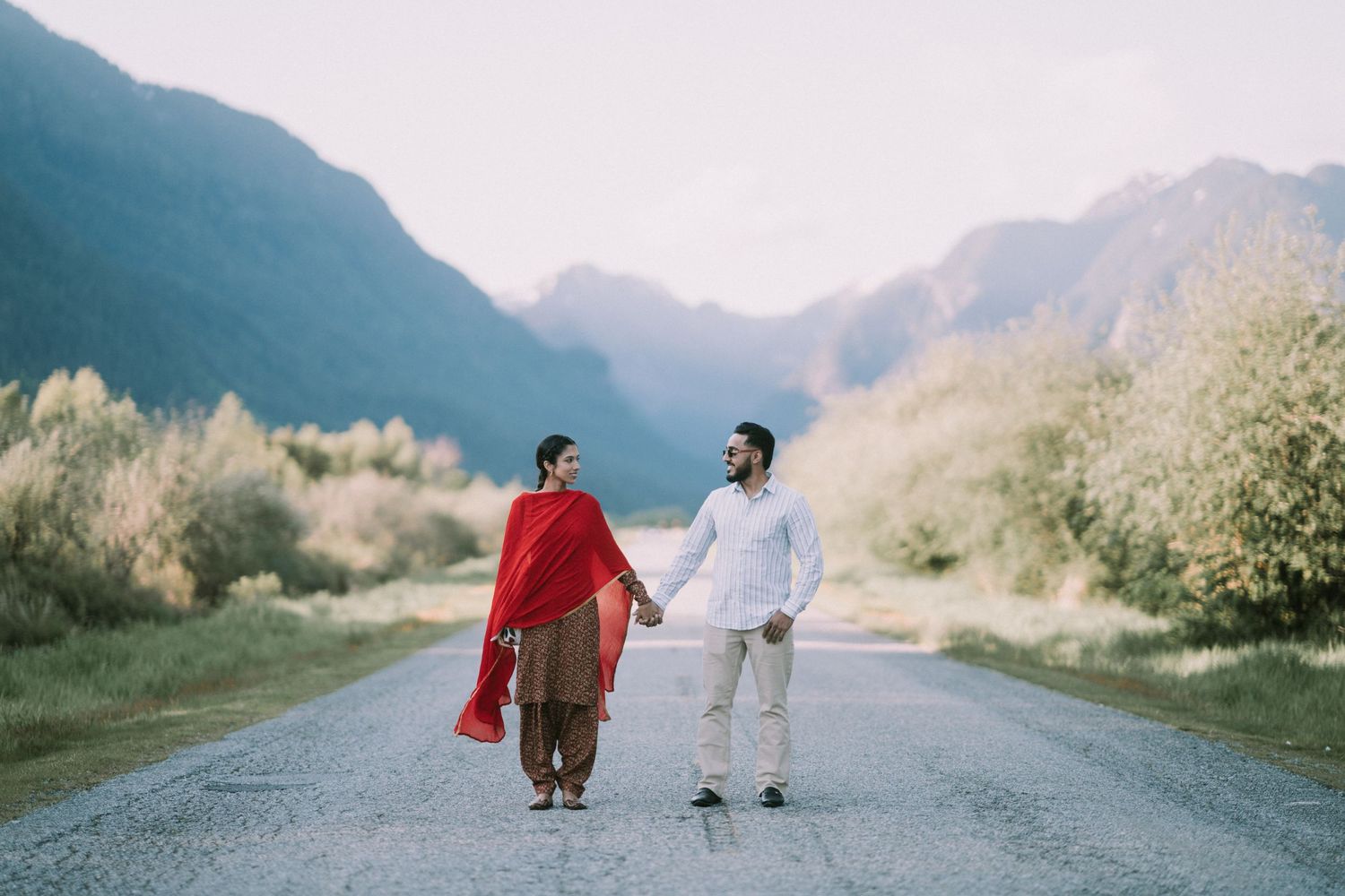 A couple in red and white outfits sits on a winding mountain road during sunset.