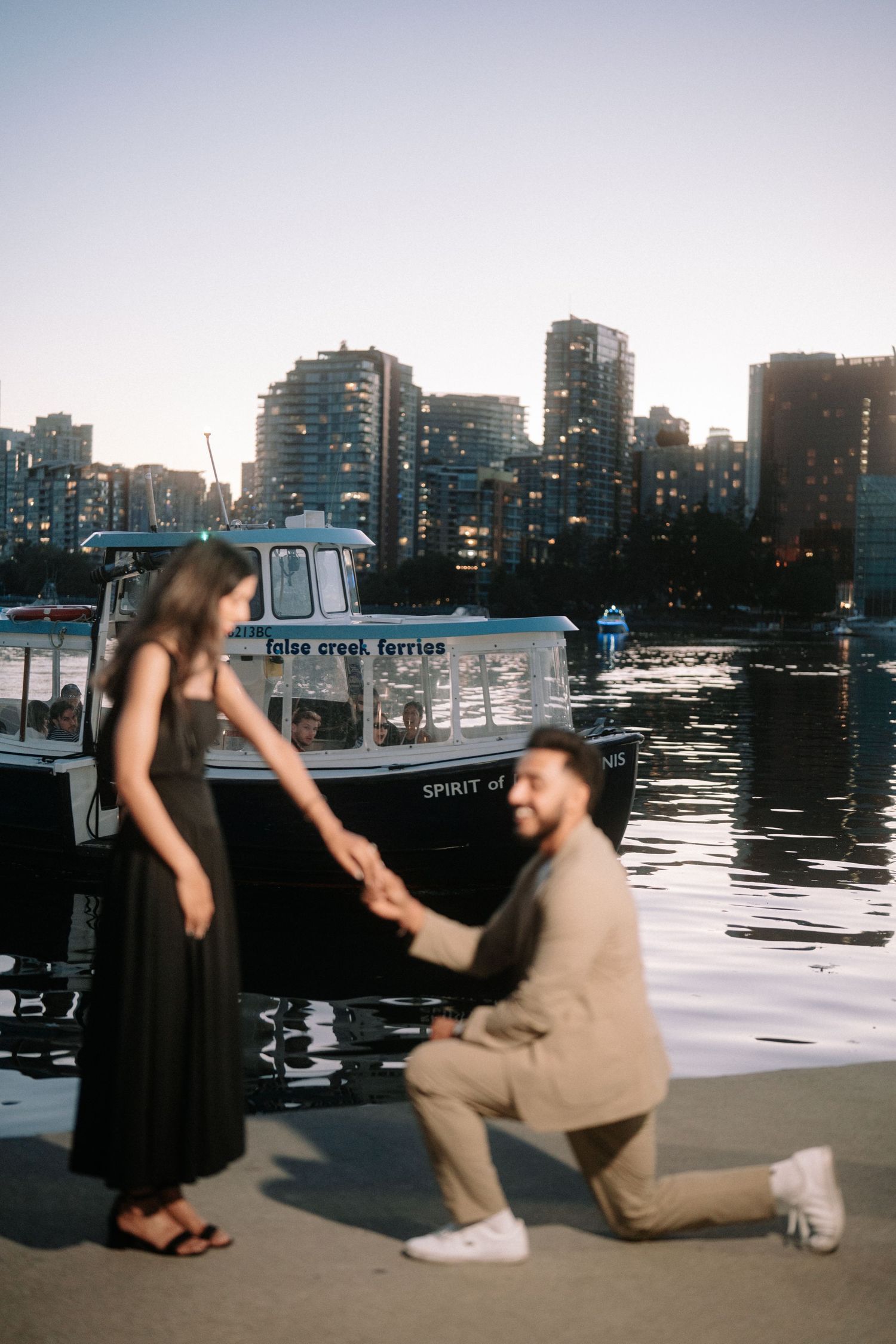A sequence of silhouettes against a waterfront cityscape shows a romantic proposal moment unfolding at sunset.