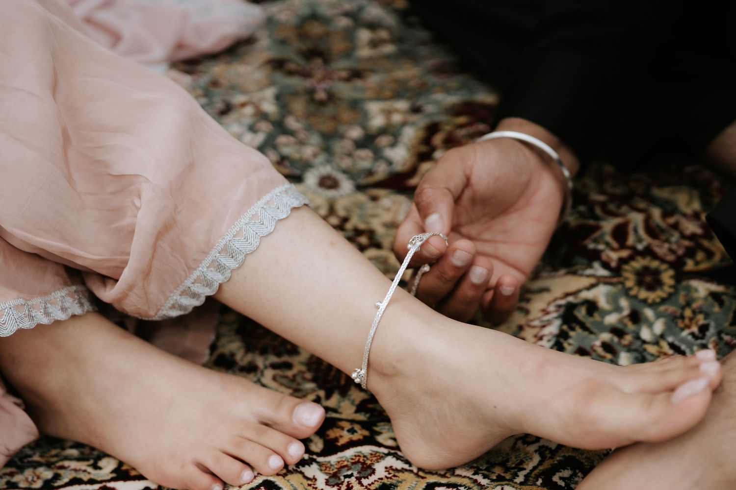 Close-up of hands with jewelry and delicate details on a patterned rug.
