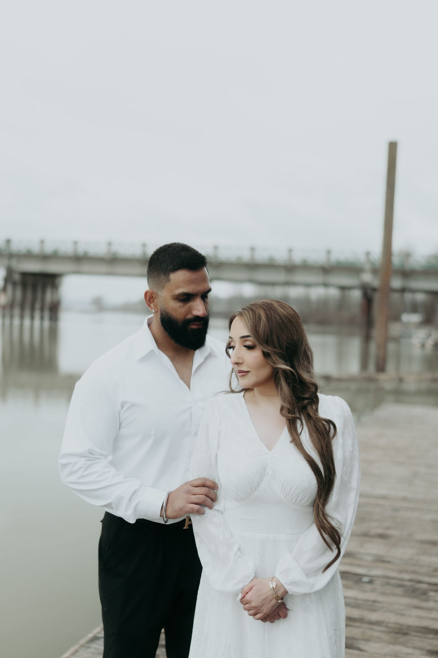 A couple embraces on a foggy dock wearing coordinating white outfits.
