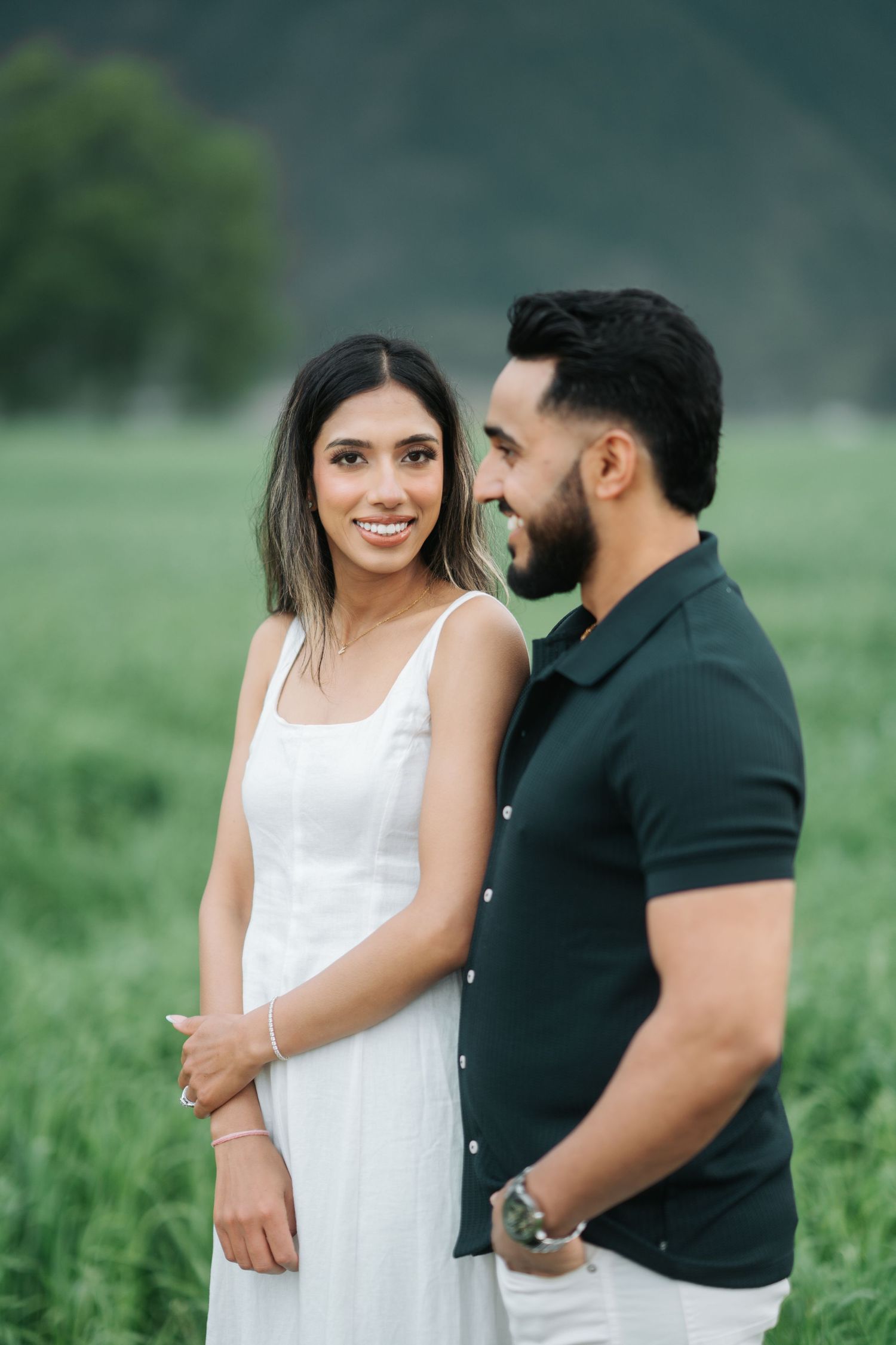A couple shares intimate moments in a green field during a romantic outdoor photo session.