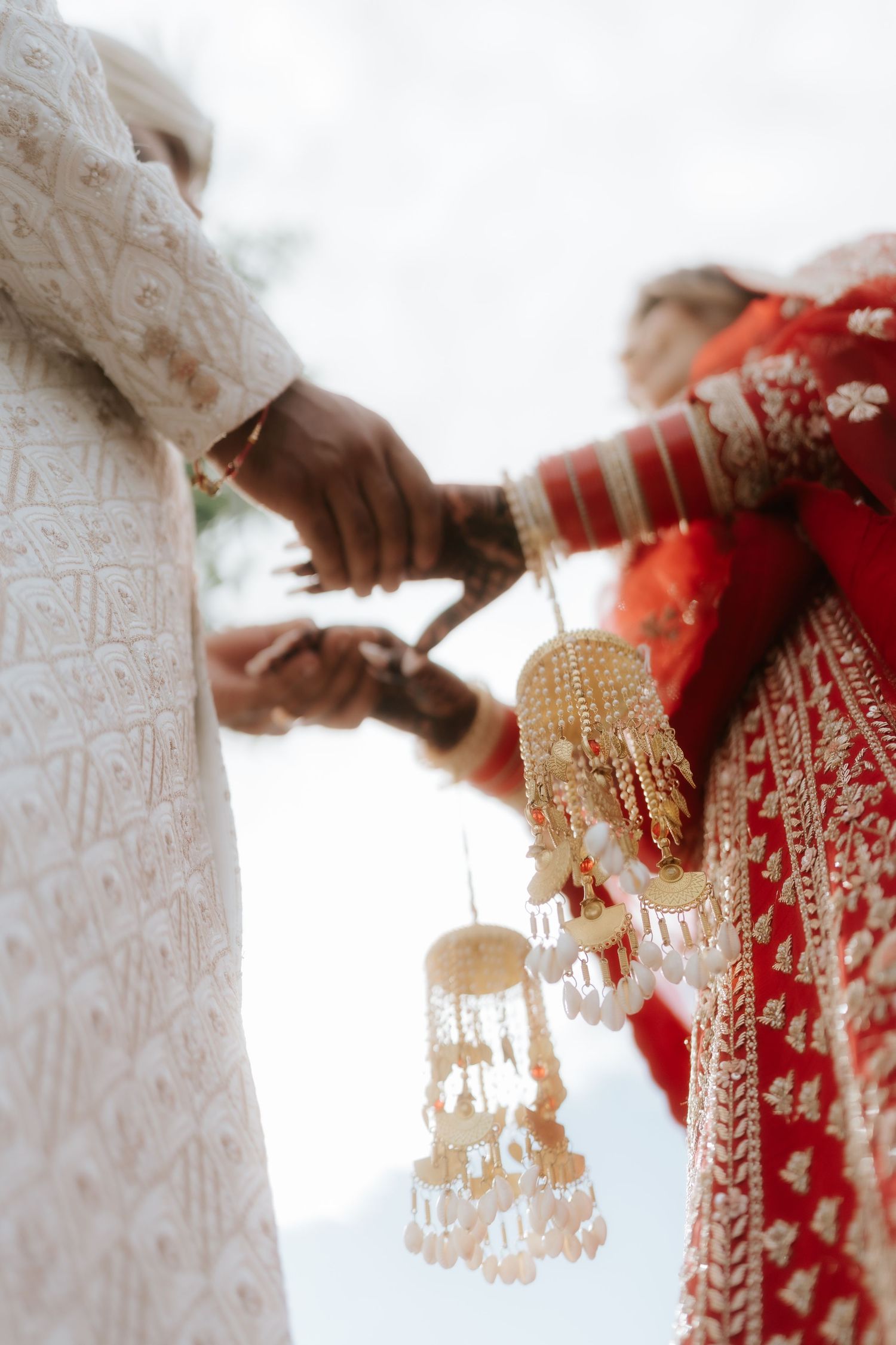 Indian bride in red lehenga and groom in white sherwani exchange kalire during traditional Hindu wedding ceremony.