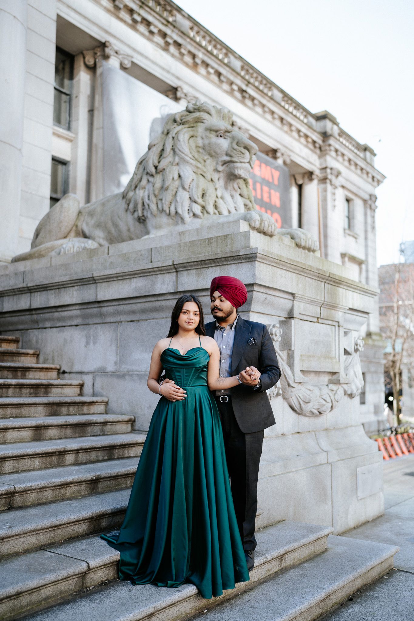 Couple shares romantic moment on grand stone steps of historic building in elegant emerald gown and formal attire.