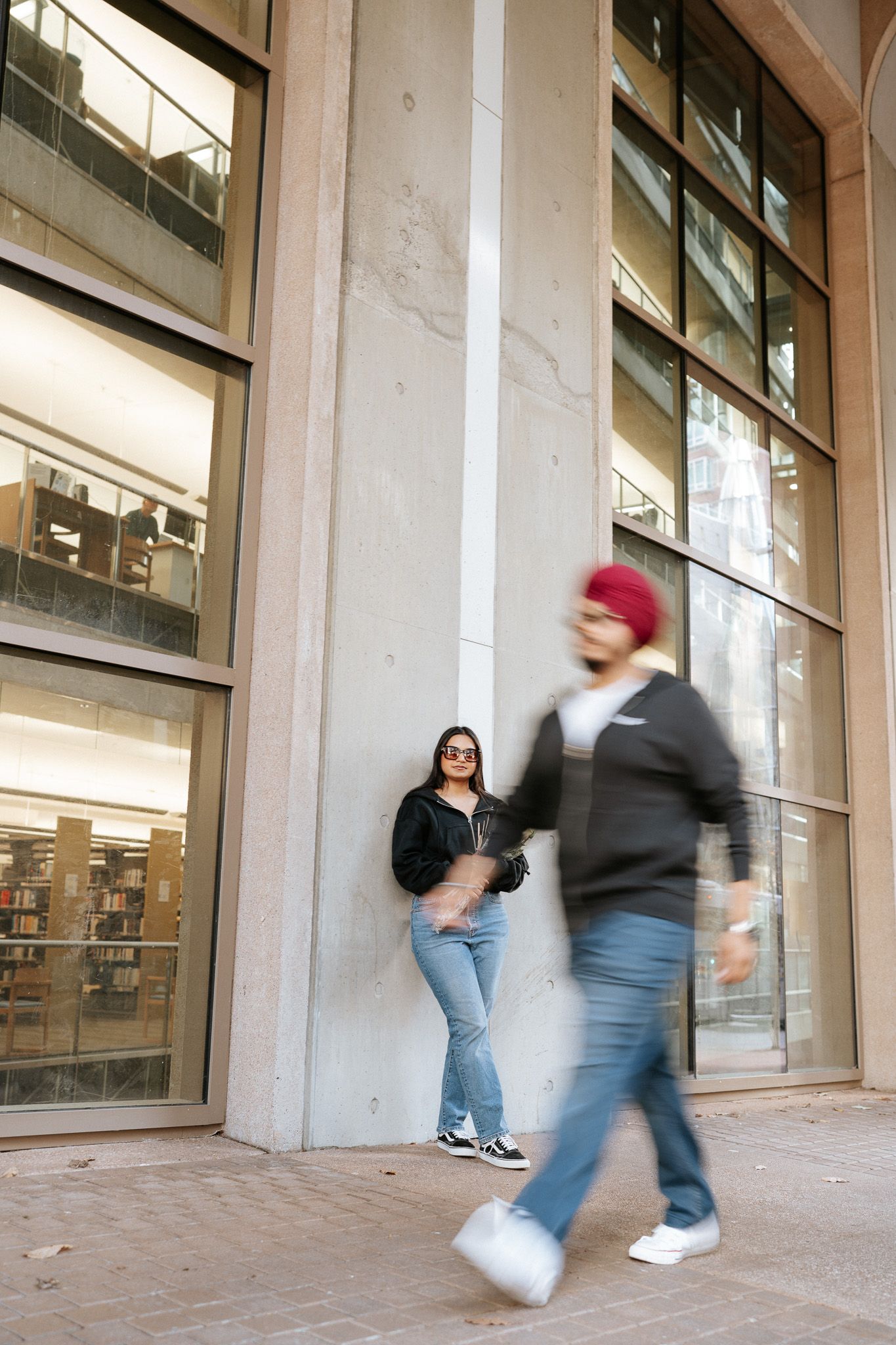 Motion blur captures people walking past large windows of a modern building entrance with concrete columns.