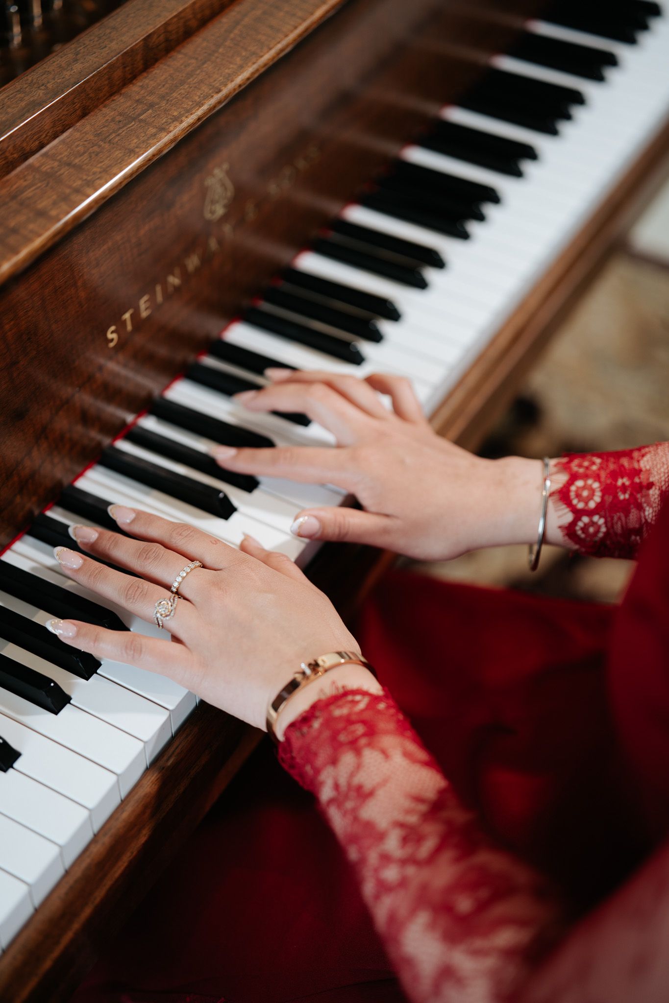 Close-up of hands with jewelry playing keys on a Steinway grand piano.