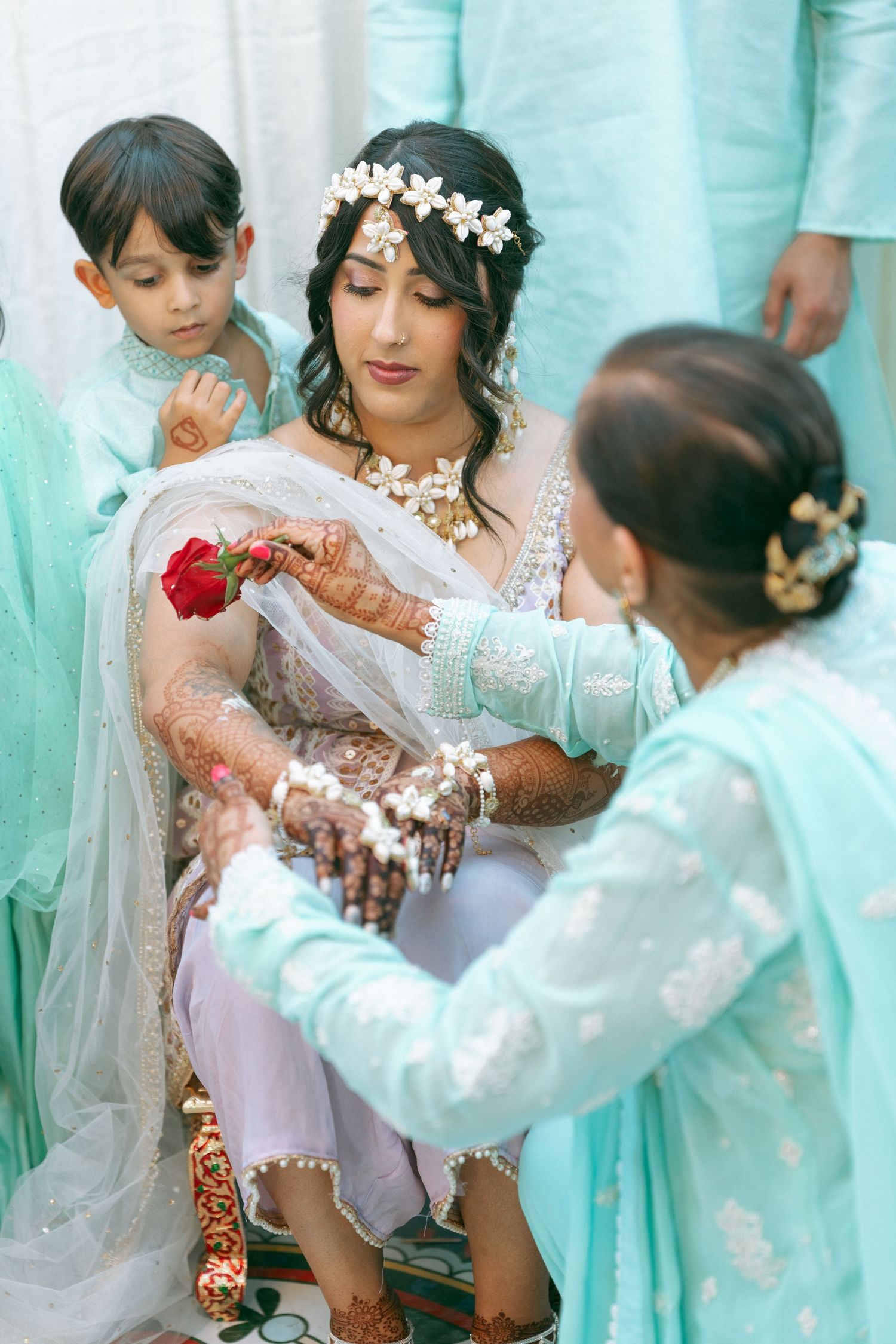 Bride in light blue lehenga with mehndi hands receives red rose during Indian wedding ceremony.