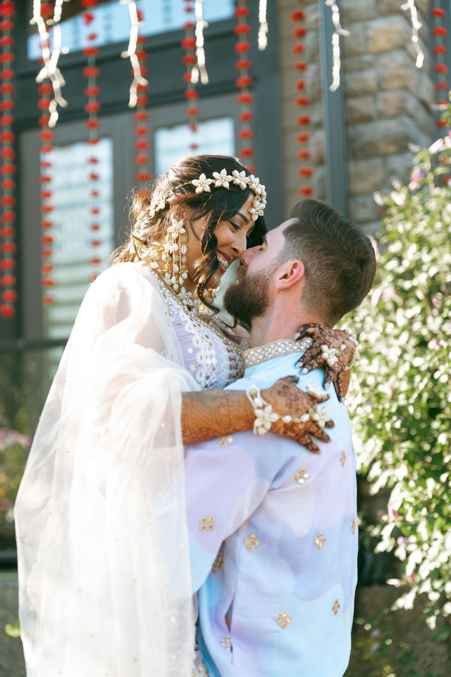 Bride and groom share a romantic kiss at a South Asian wedding ceremony, bride wearing floral headpiece and mehndi.